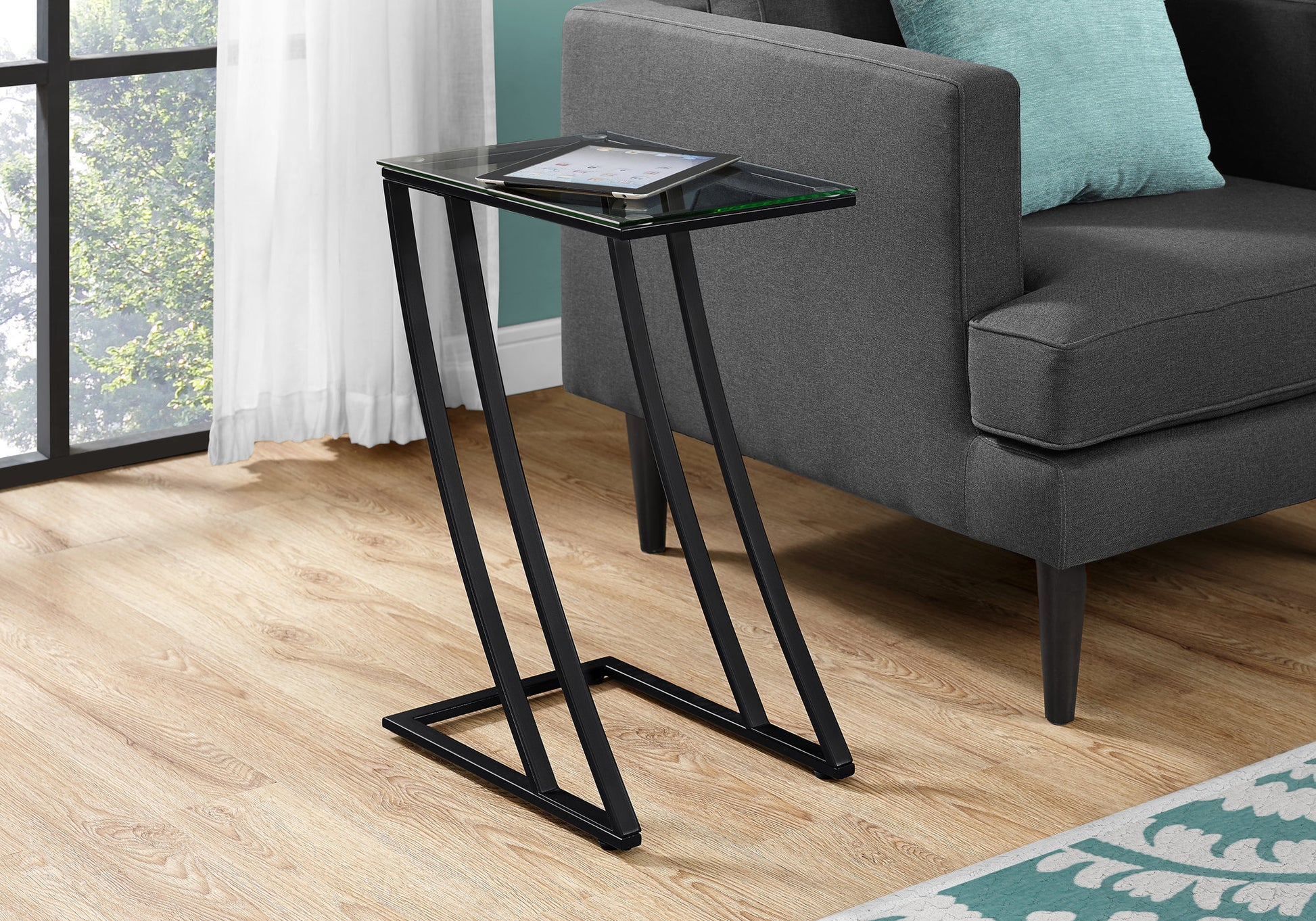 Modern black metal Ctable with clear glass top holding a tablet