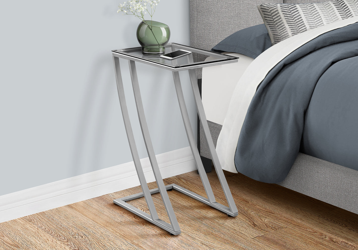 Modern Ctable with silver metal frame and clear glass top next to a bed