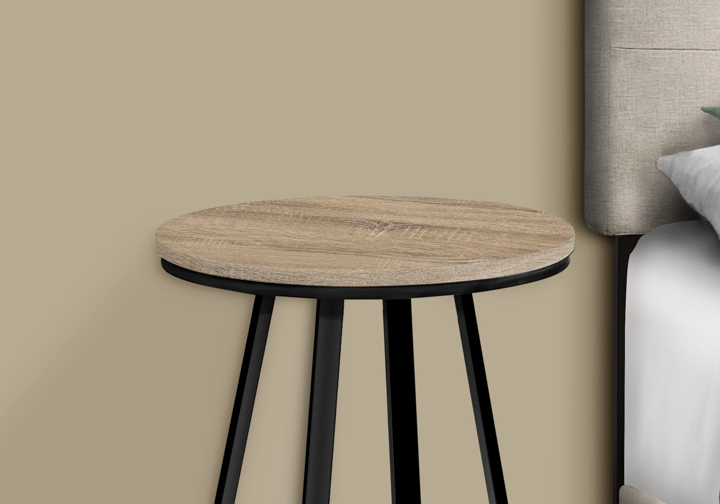 Round wood grain side table with black metal legs next to a bed