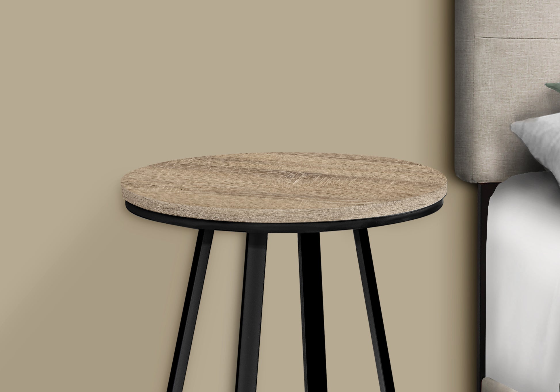 Round wood grain side table with black metal legs next to a bed