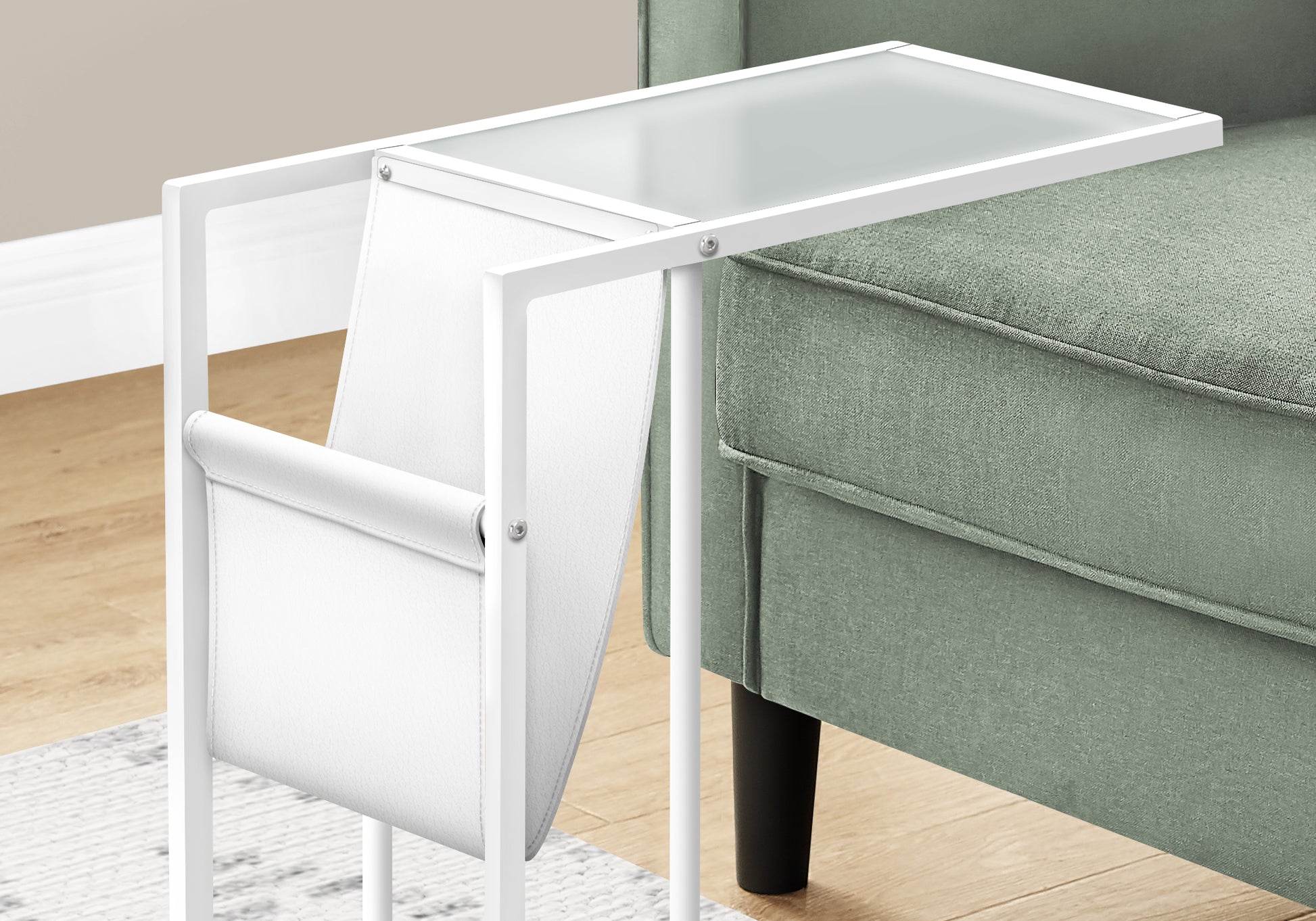 White metal C table with glass top and magazine holder beside green sofa