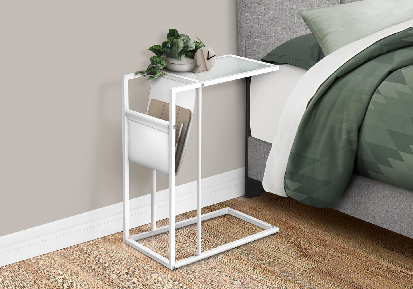 White metal Ctable with glass top and builtin magazine holder next to bed