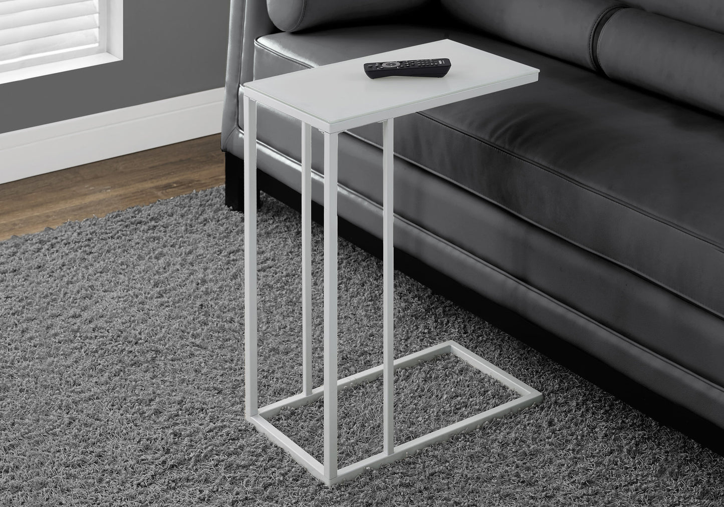 White Ctable with glass top and metal frame beside black leather sofa