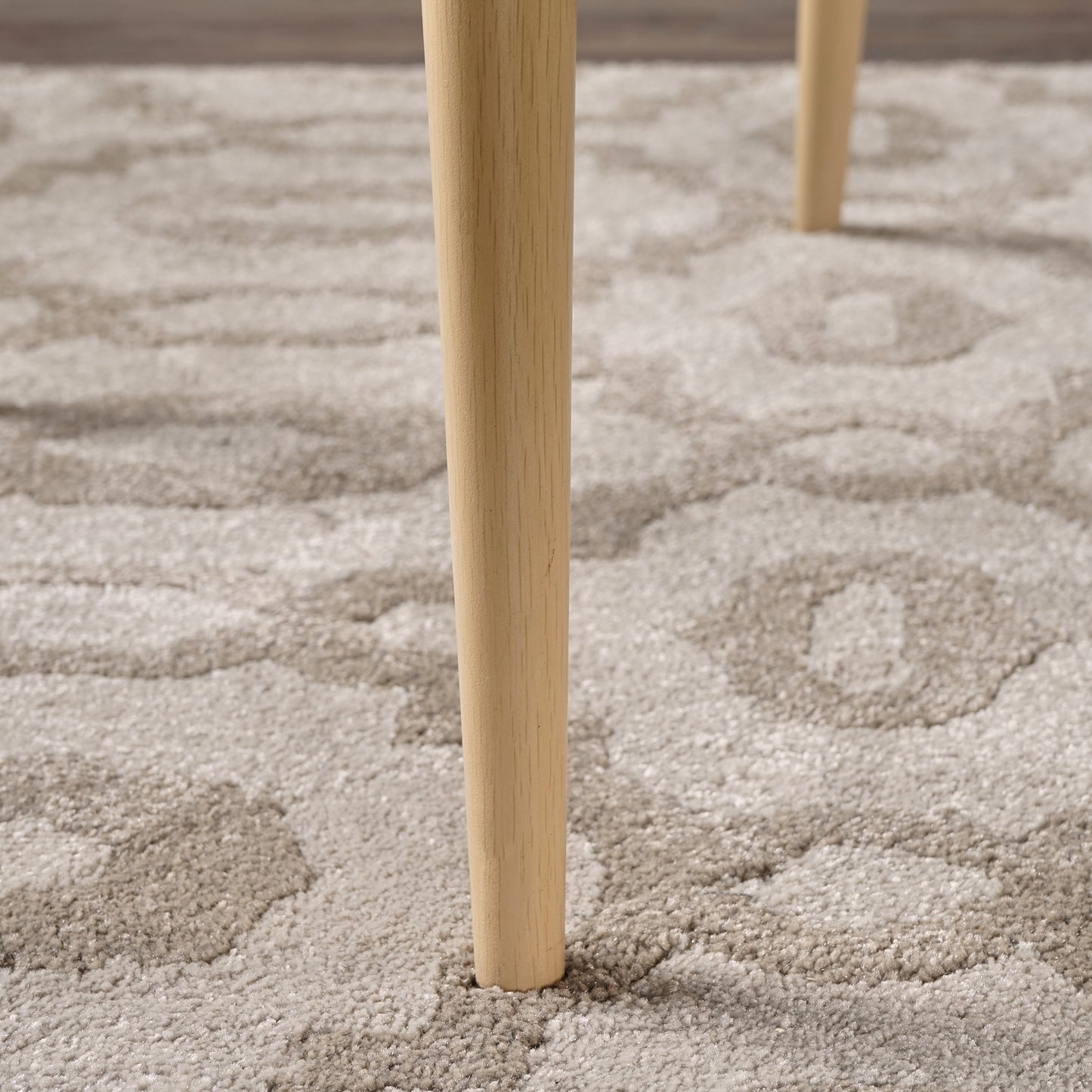 Close up of a light oak wood table leg resting on a beige patterned area rug