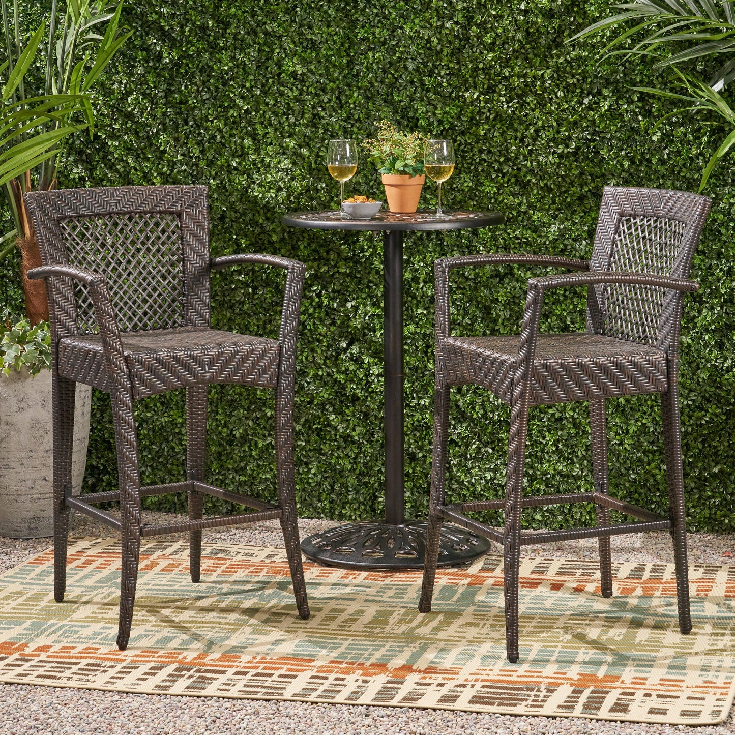 Two dark brown rattan bar stools with armrests a small round bistro table and two glasses of wine outdoors