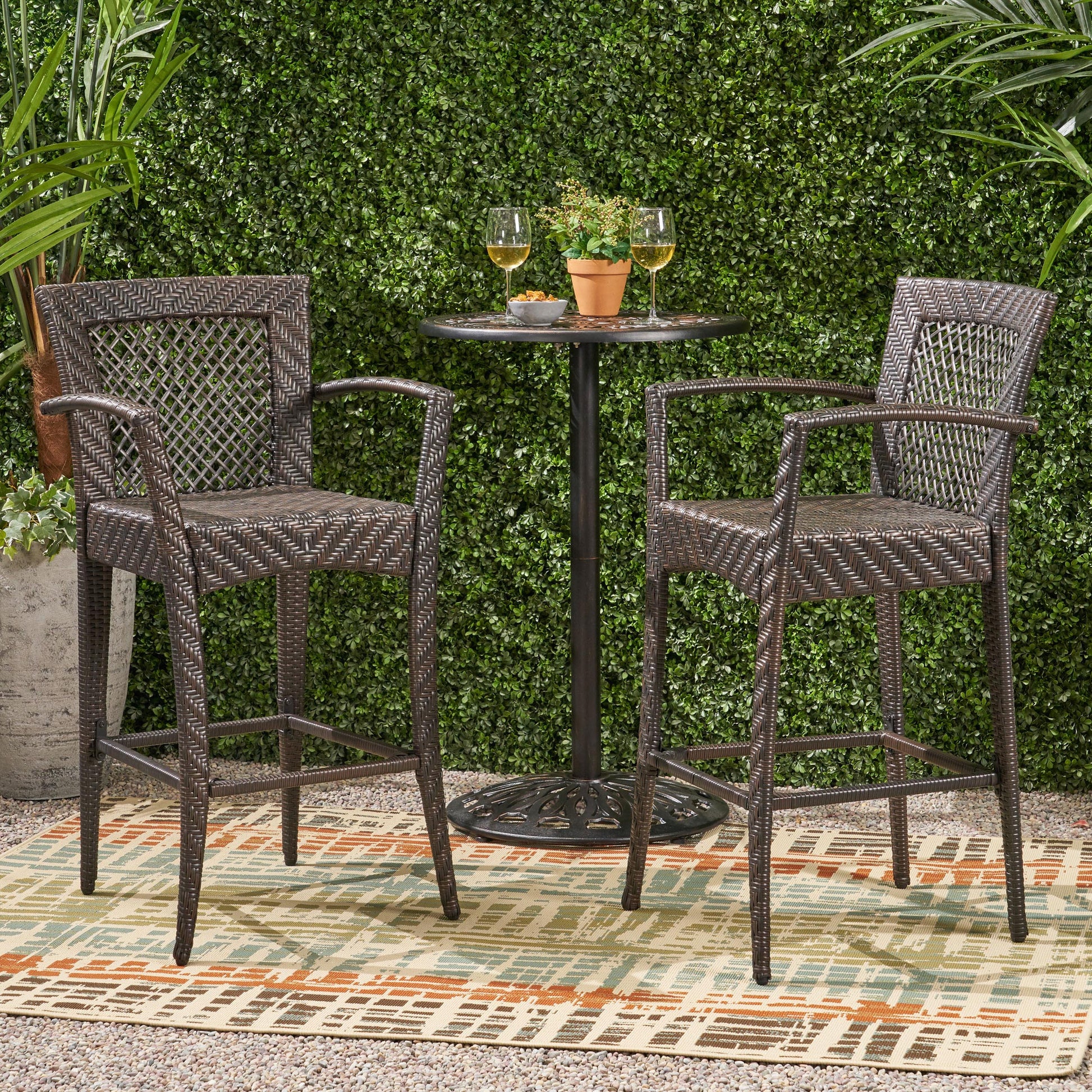 Two dark brown rattan bar stools with armrests a small round bistro table and two glasses of wine outdoors