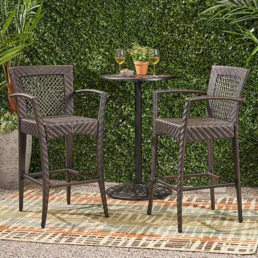 Two dark brown rattan bar stools with armrests a small round bistro table and two glasses of wine outdoors