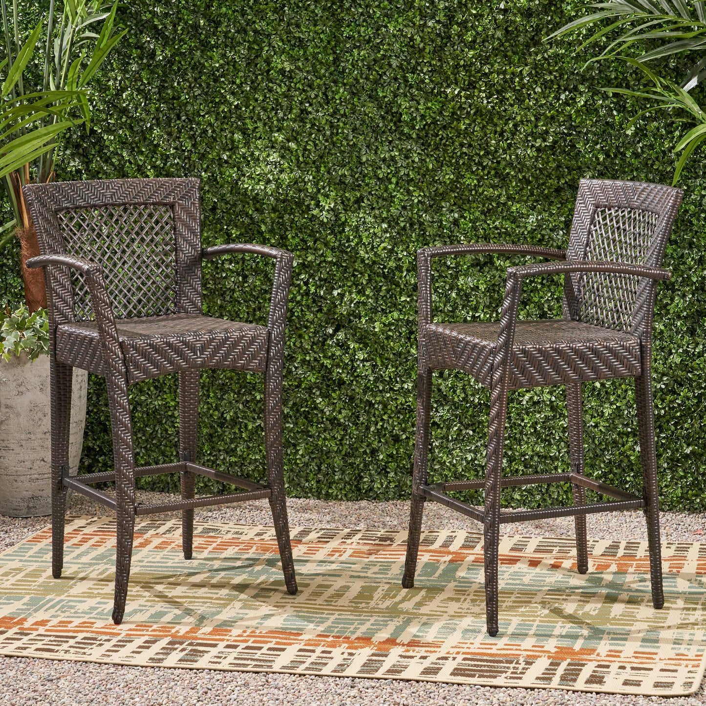 Two dark brown wicker bar stools with woven backrests stand on a patio rug