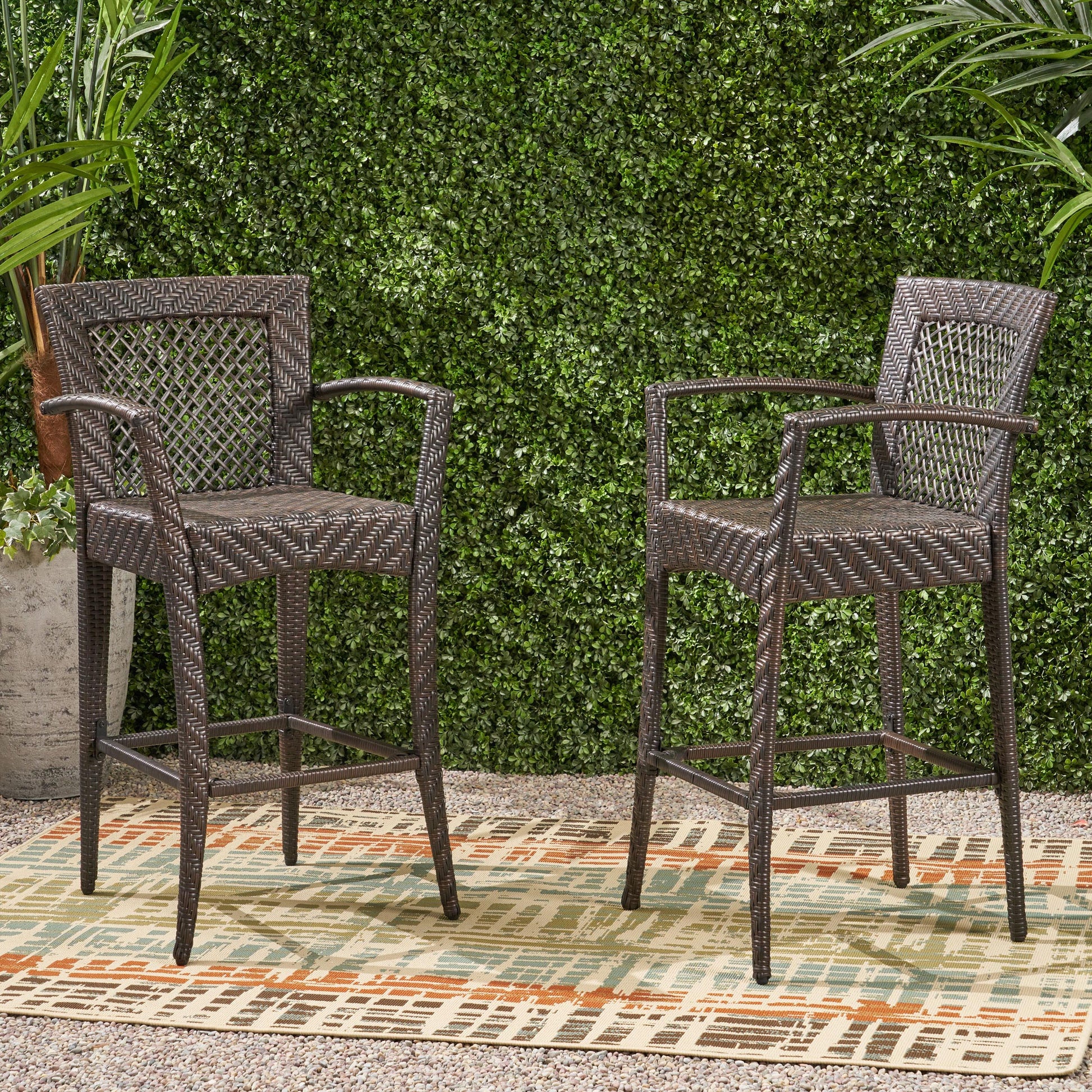 Two dark brown wicker bar stools with woven backrests stand on a patio rug