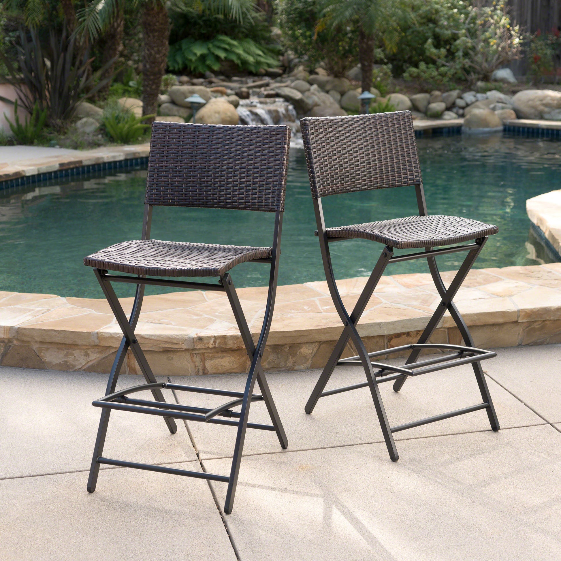 Two dark brown wicker bar stools with metal frames are placed on a patio by a pool