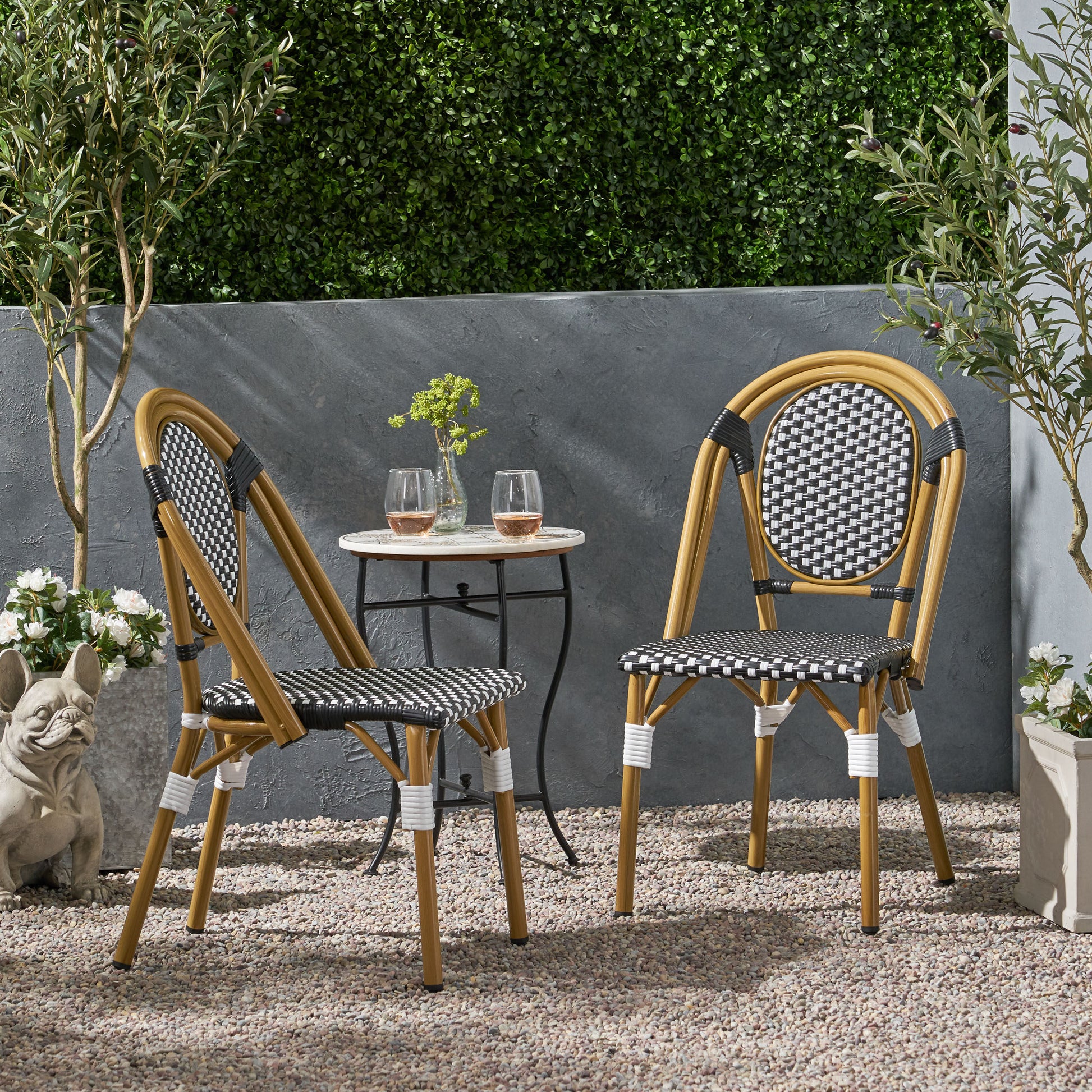 Two black and white rattan bistro chairs with bamboo frames sit on a gravel patio