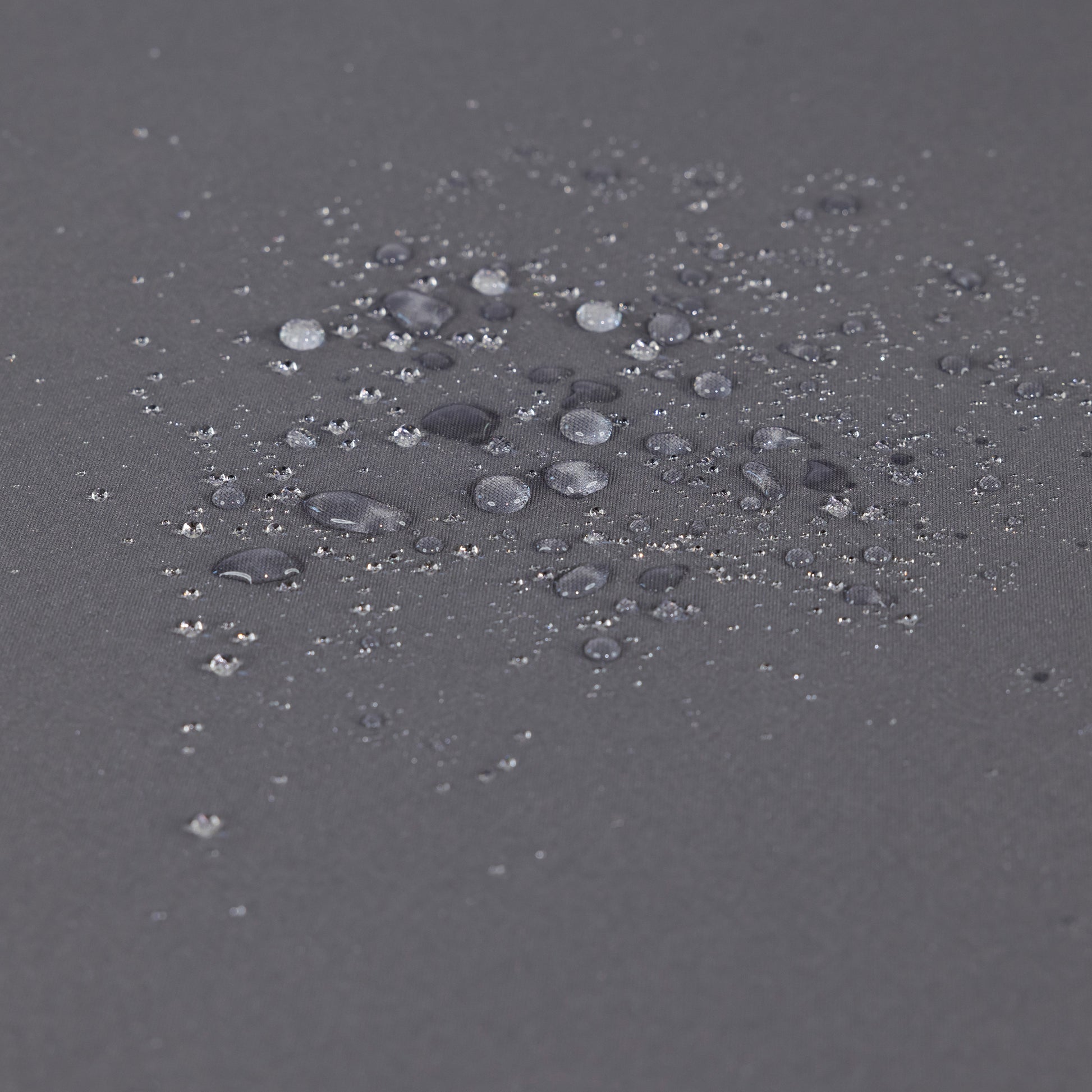 Closeup of dark grey fabric showing water beads on its waterproof surface