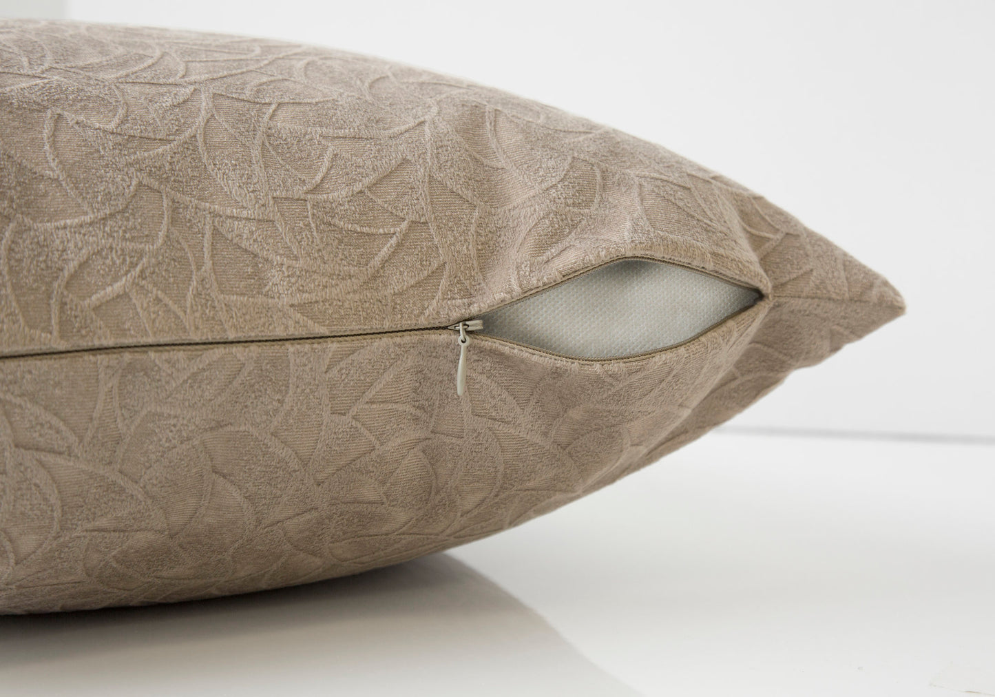 Taupe textured cushion with an embossed leaf pattern and visible zipper closure