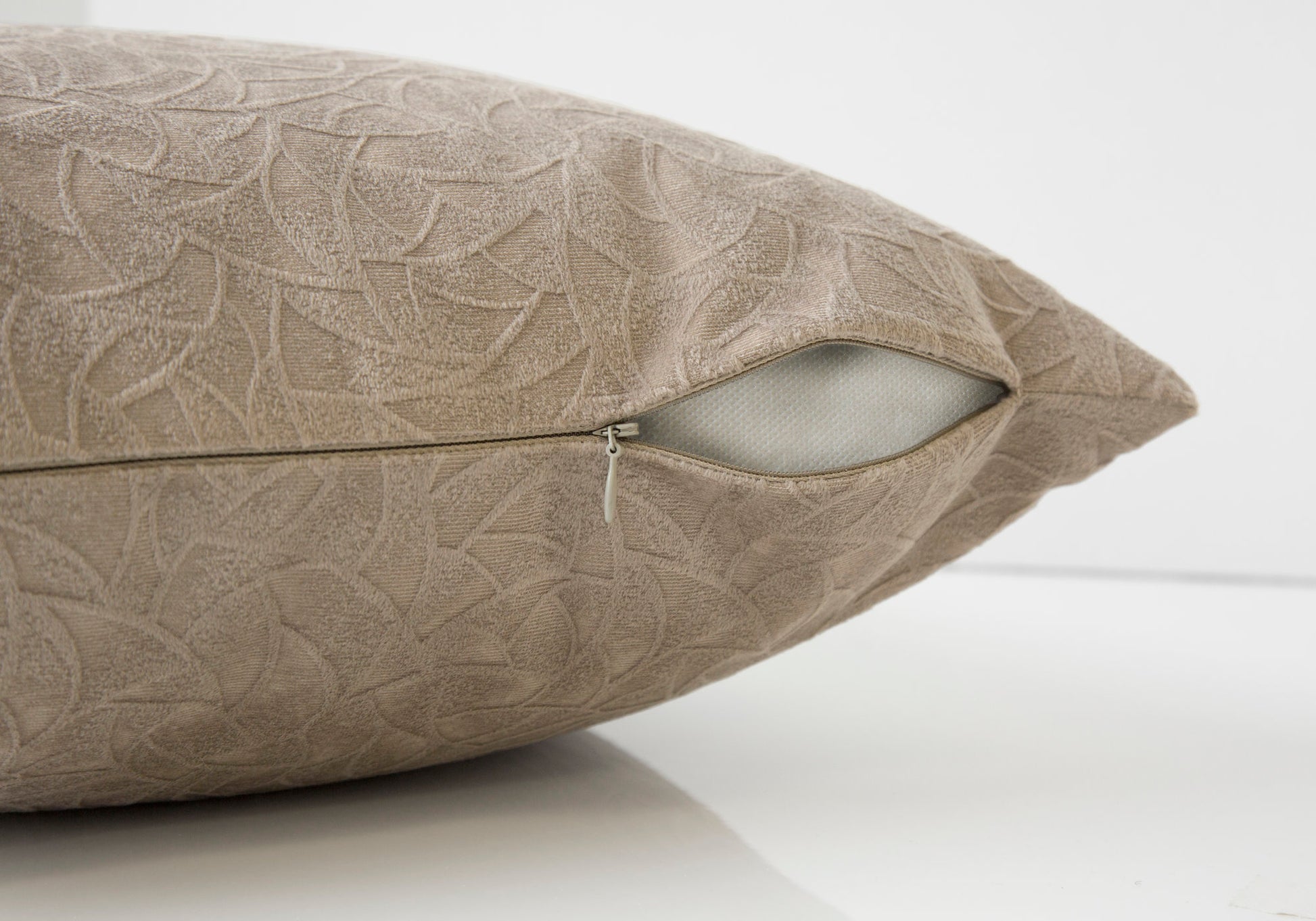 Taupe textured cushion with an embossed leaf pattern and visible zipper closure