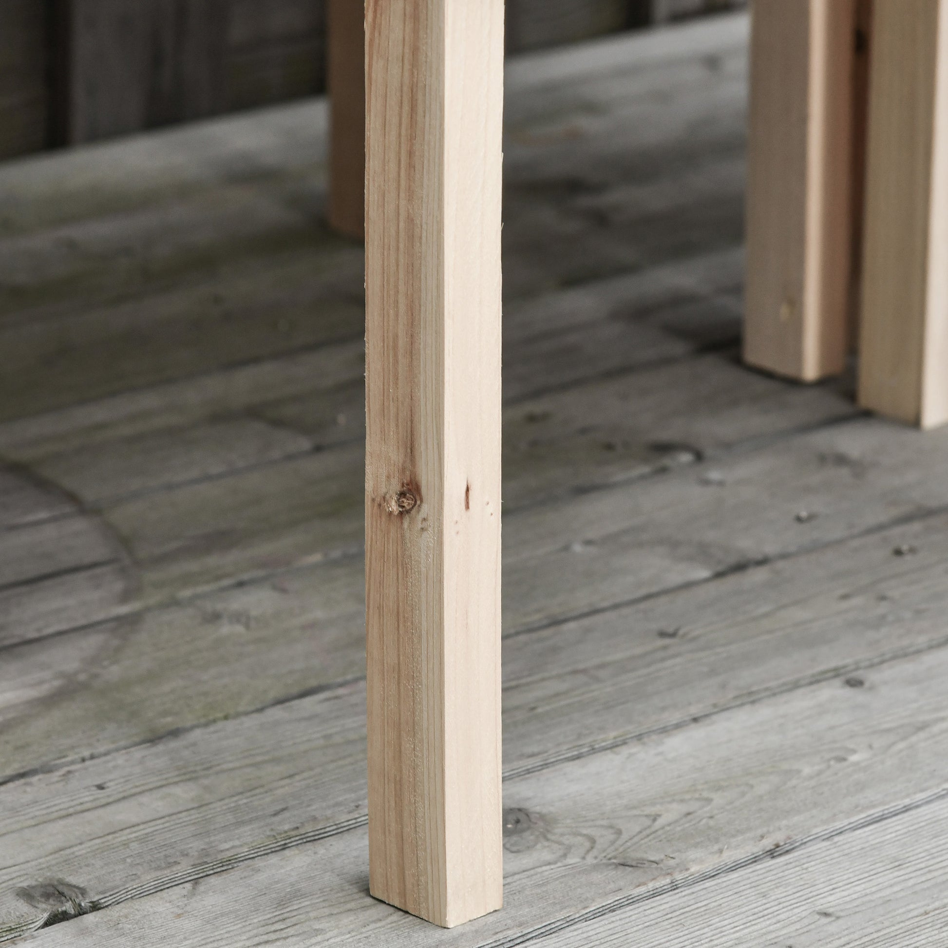 Close up of a light wood table leg on a grey wooden deck showing natural grain