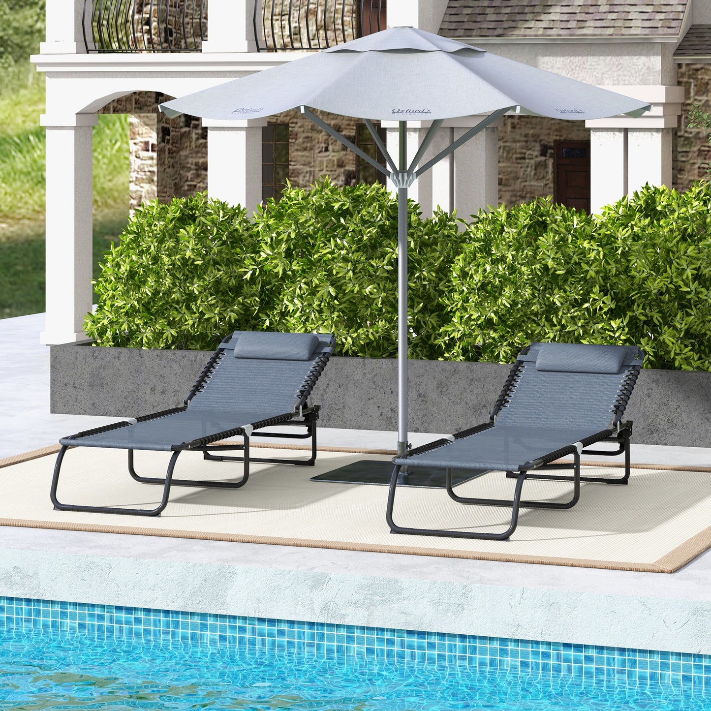 Two gray adjustable chaise lounge chairs with headrests by a poolside patio under a large light gray patio umbrella