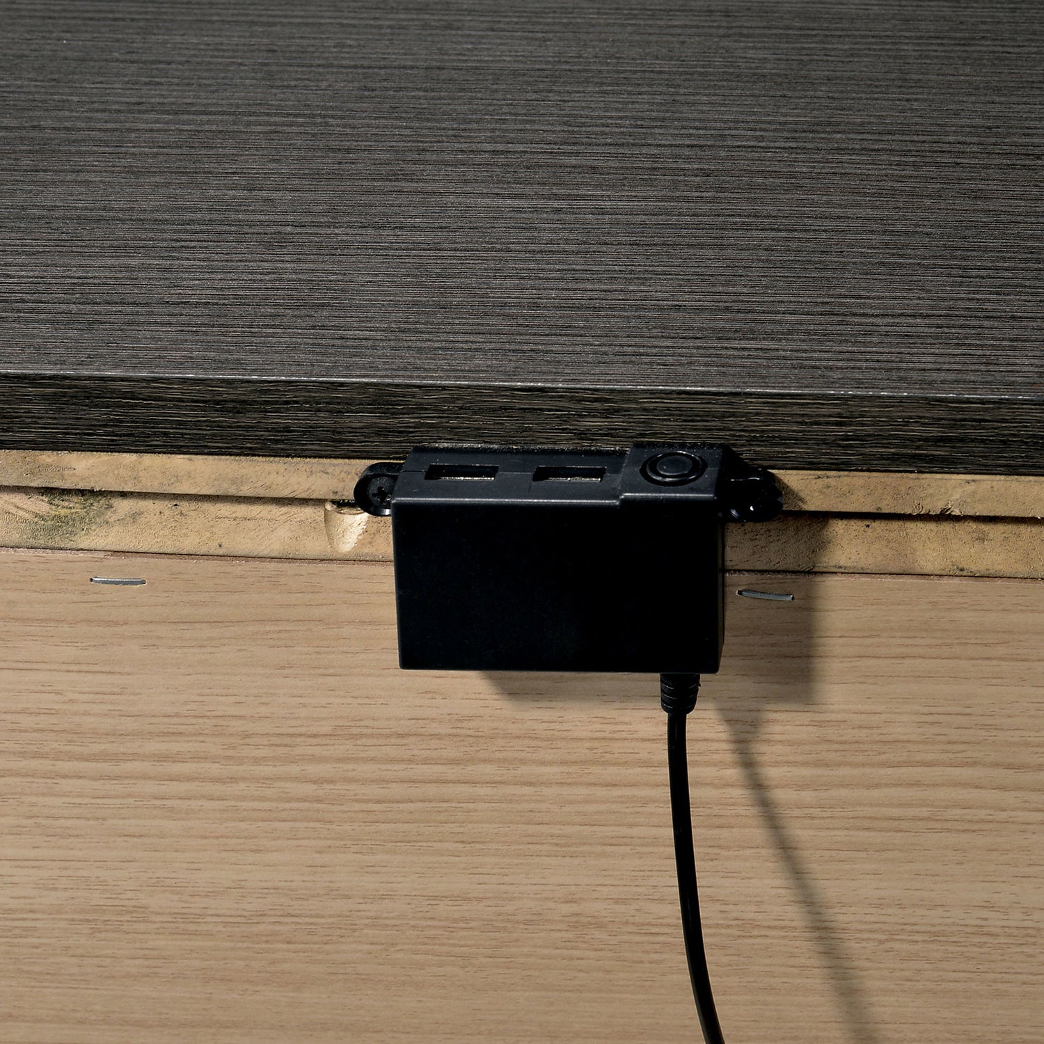 Black power adapter with dual USB ports attached to furniture