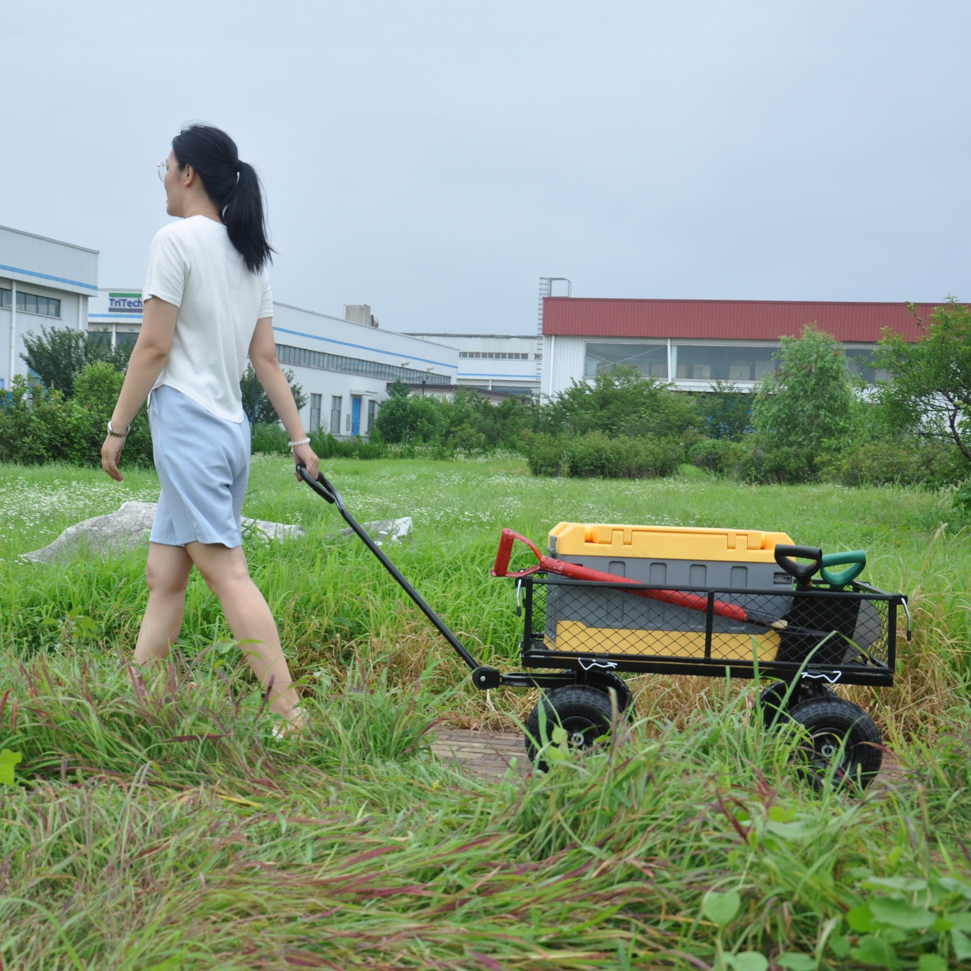 Yellow and gray cooler cart with red shovel and green handle pulled by a woman