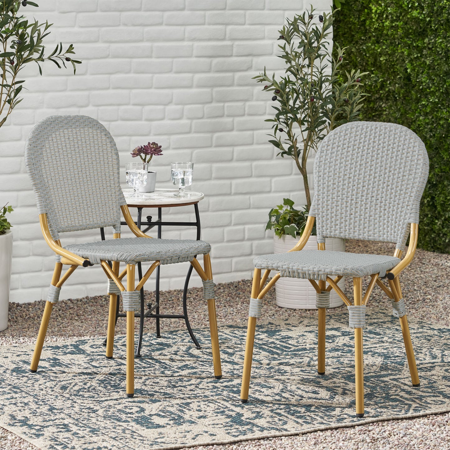 Pair of grey woven bistro chairs with golden legs on an outdoor patio rug