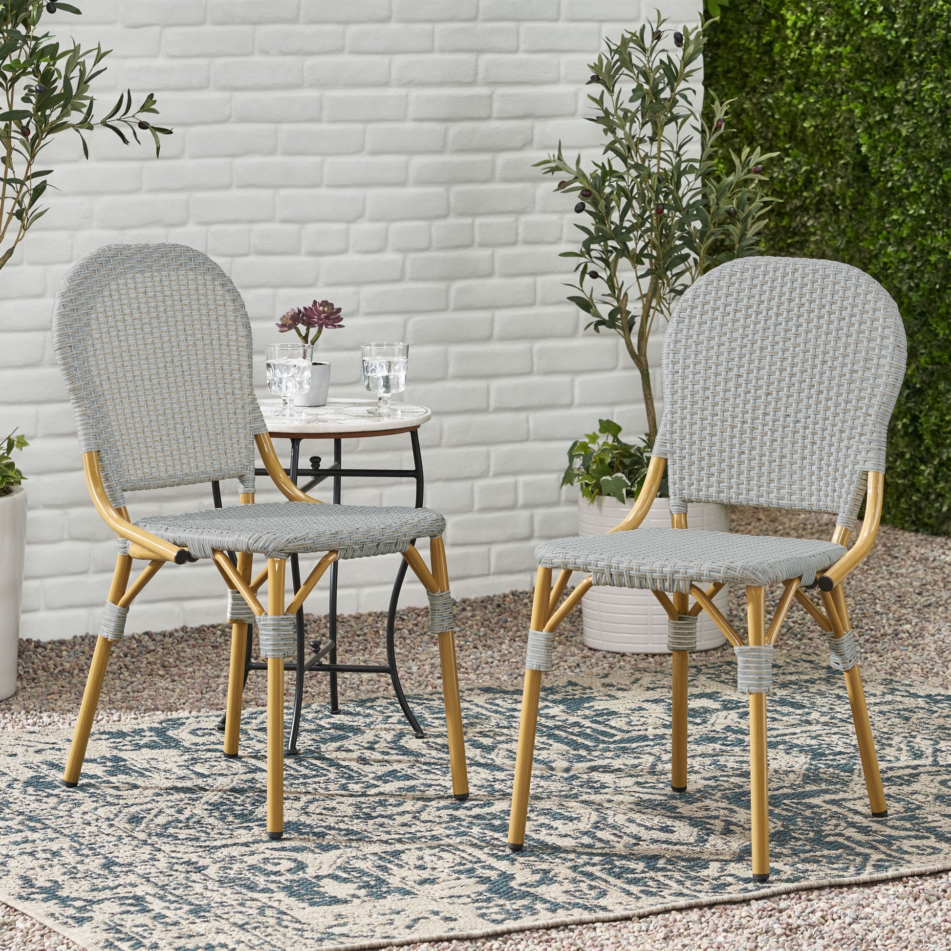 Pair of grey woven bistro chairs with golden legs on an outdoor patio rug
