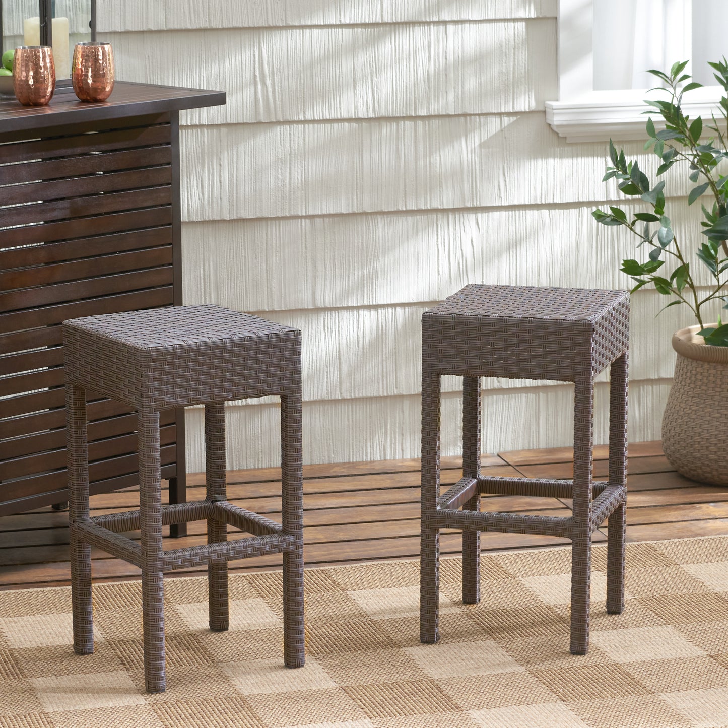Two brown woven bar stools on a patio with a wood deck and plaid rug