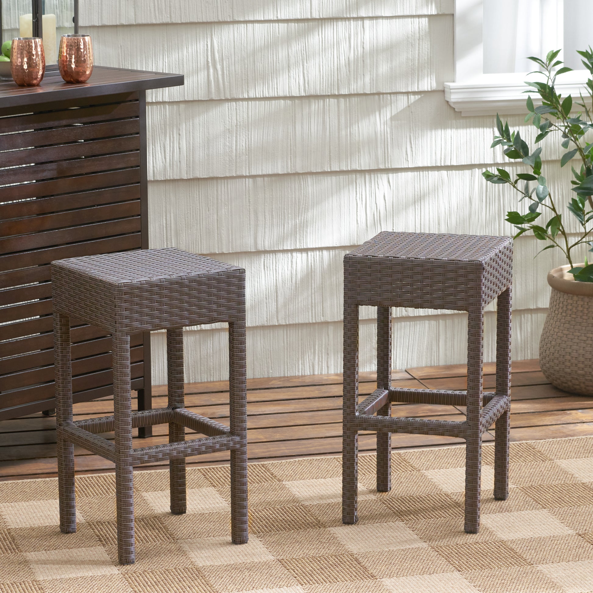 Two brown woven bar stools on a patio with a wood deck and plaid rug