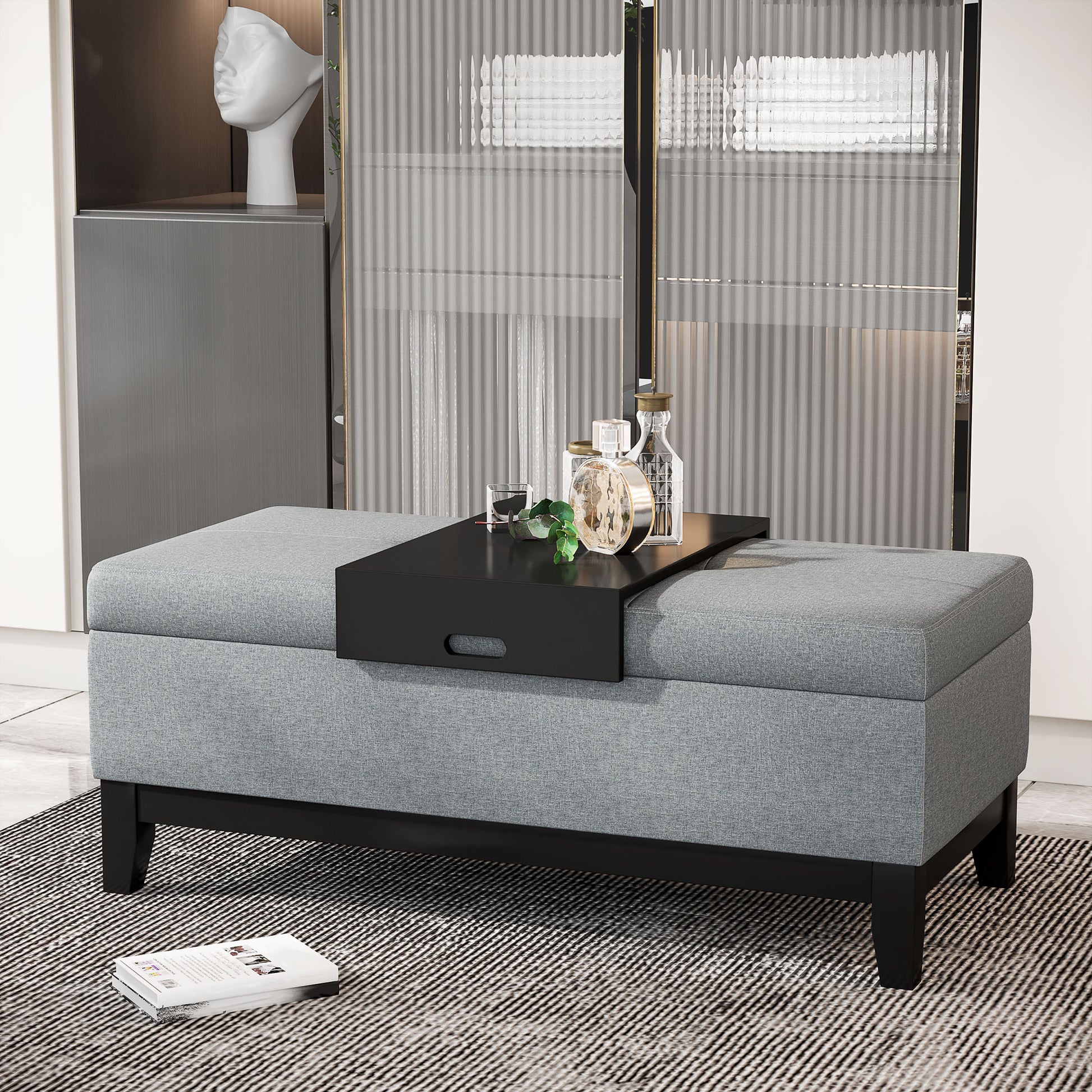Grey fabric storage ottoman with a black tray glass and decorative bottles