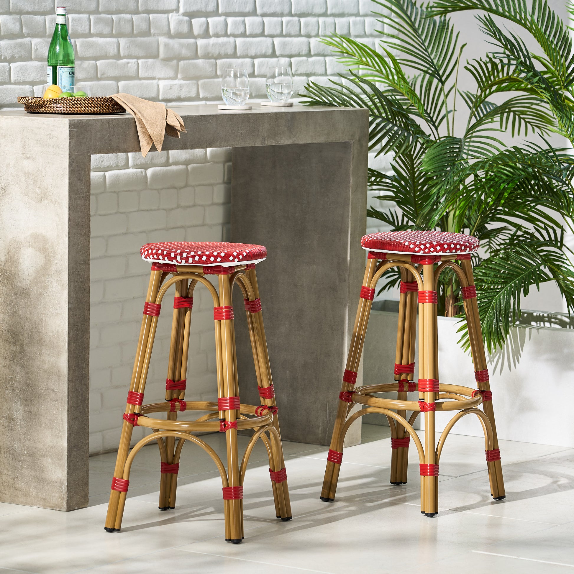 Two natural rattan bar stools with red and white woven seats in a patio setting