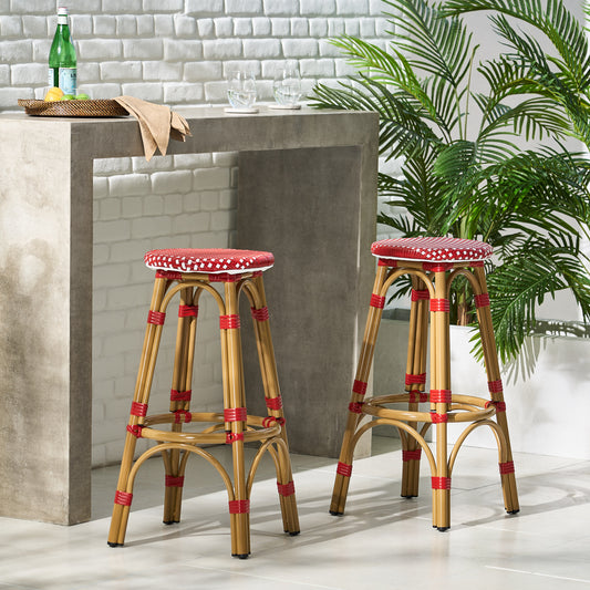 Two natural rattan bar stools with red and white woven seats in a patio setting