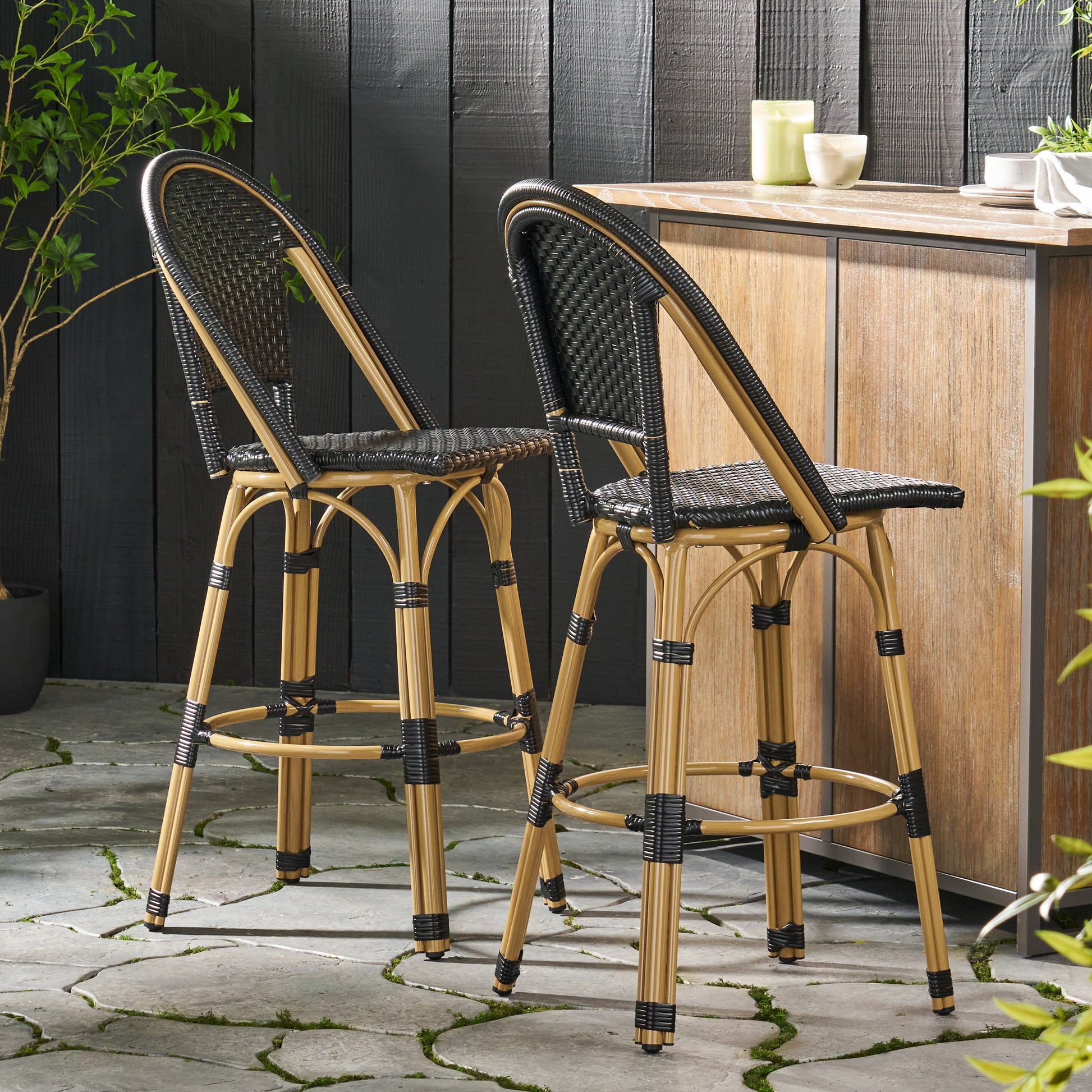 Pair of black woven rattan bar stools with natural woodcolored legs on outdoor patio