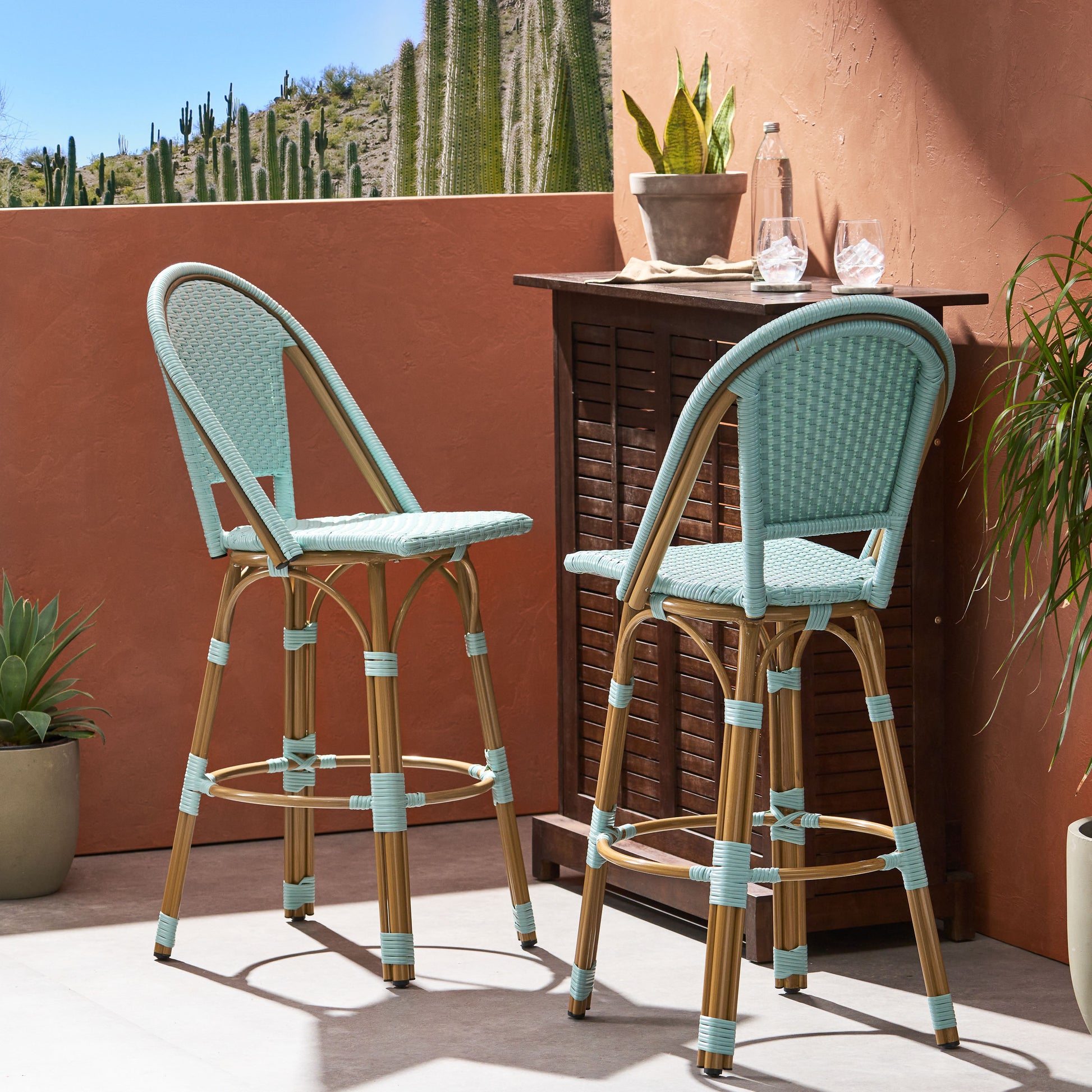 Two light blue rattan bar stools with bamboo legs on a patio with desert plants