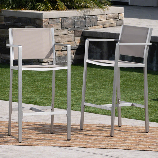 Two modern silver aluminum bar stools with beige fabric seats on an outdoor patio