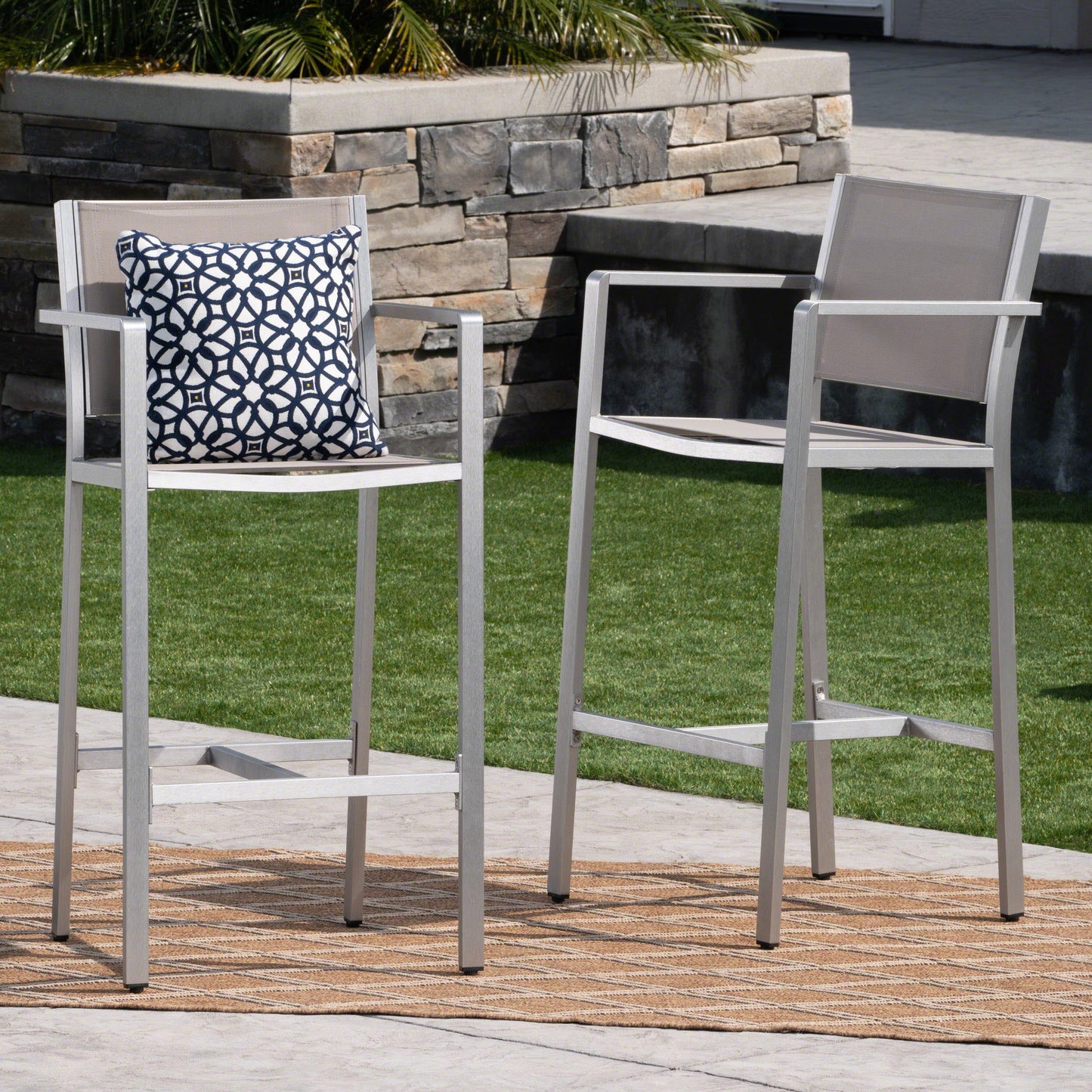 Silver aluminum bar stool with beige mesh seat and patterned outdoor pillow