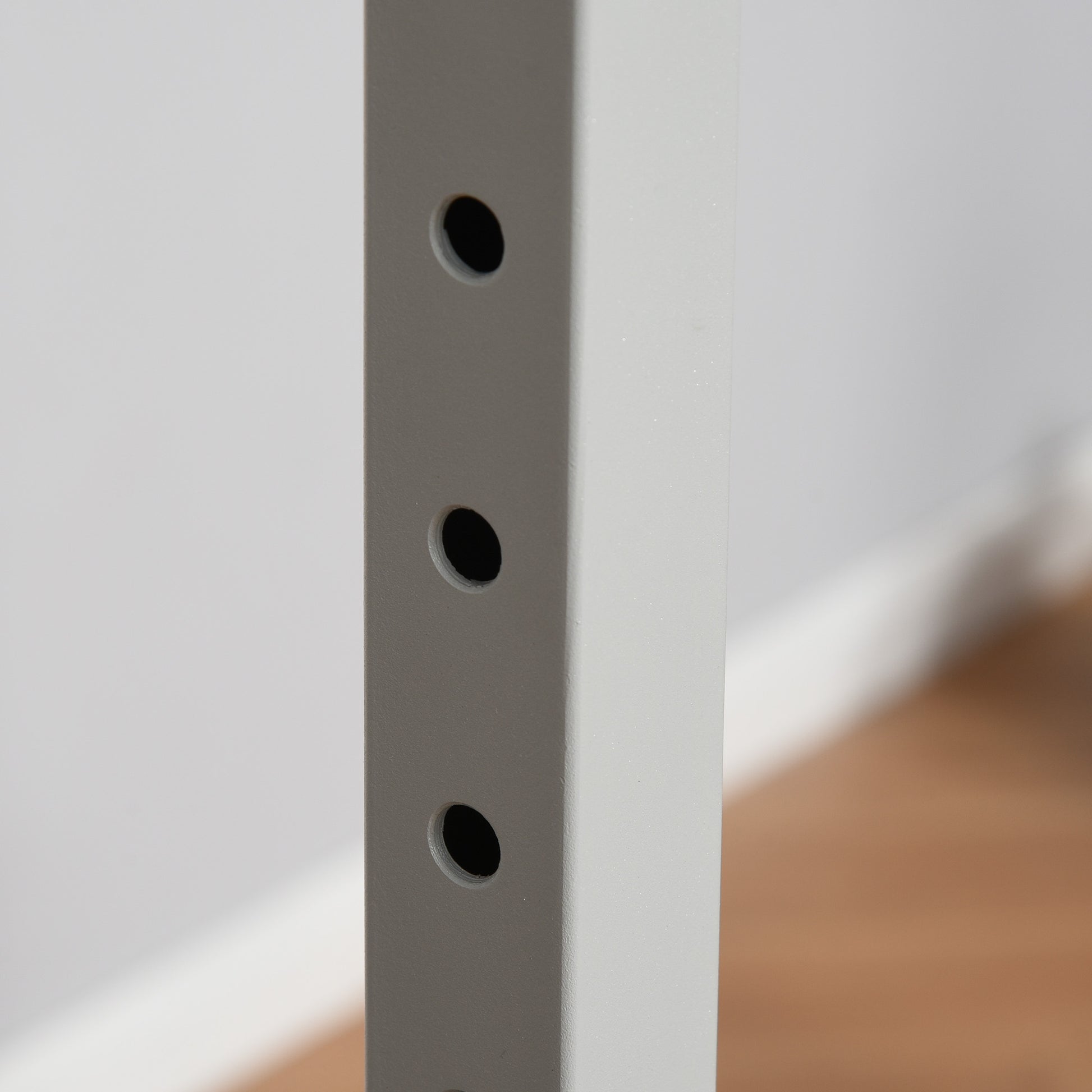 Closeup of a white metal shelf support with three predrilled holes for adjustable shelves