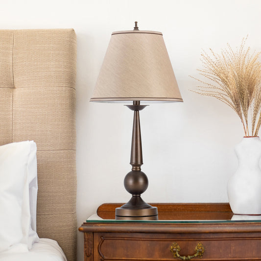 Bronze bedside lamp with a tan fabric shade featuring a decorative pedestal base