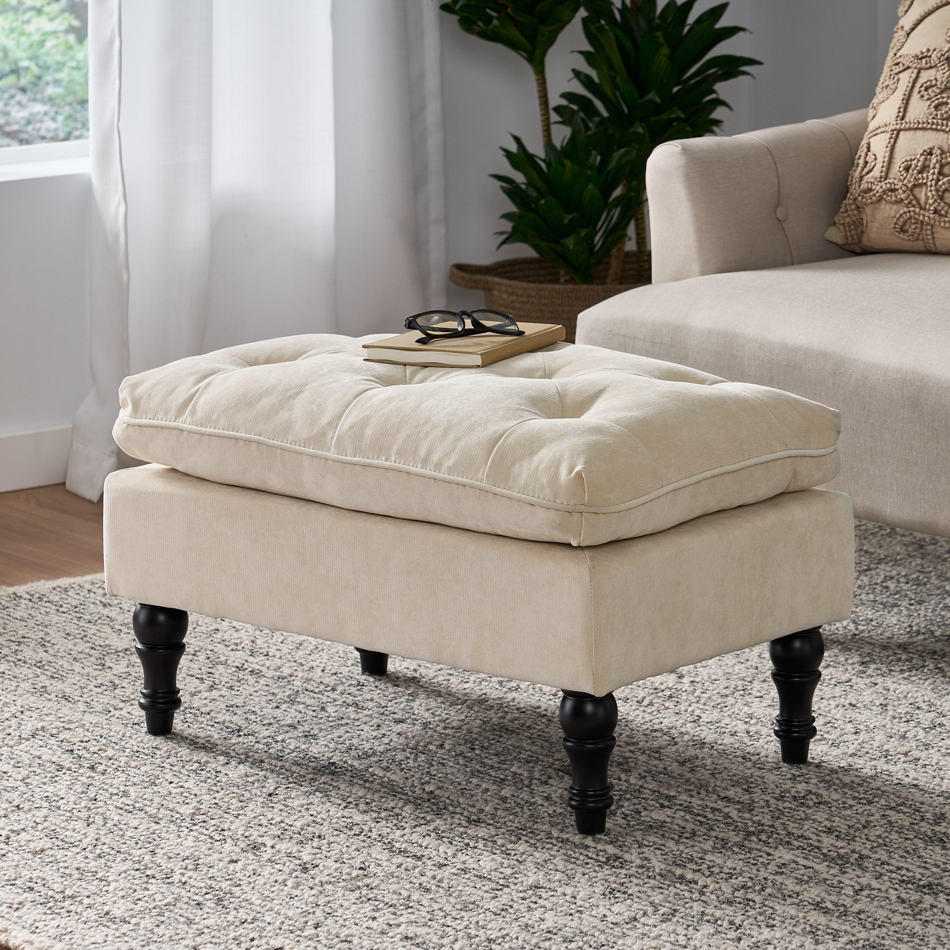Cream upholstered ottoman with tufted top and dark wood legs