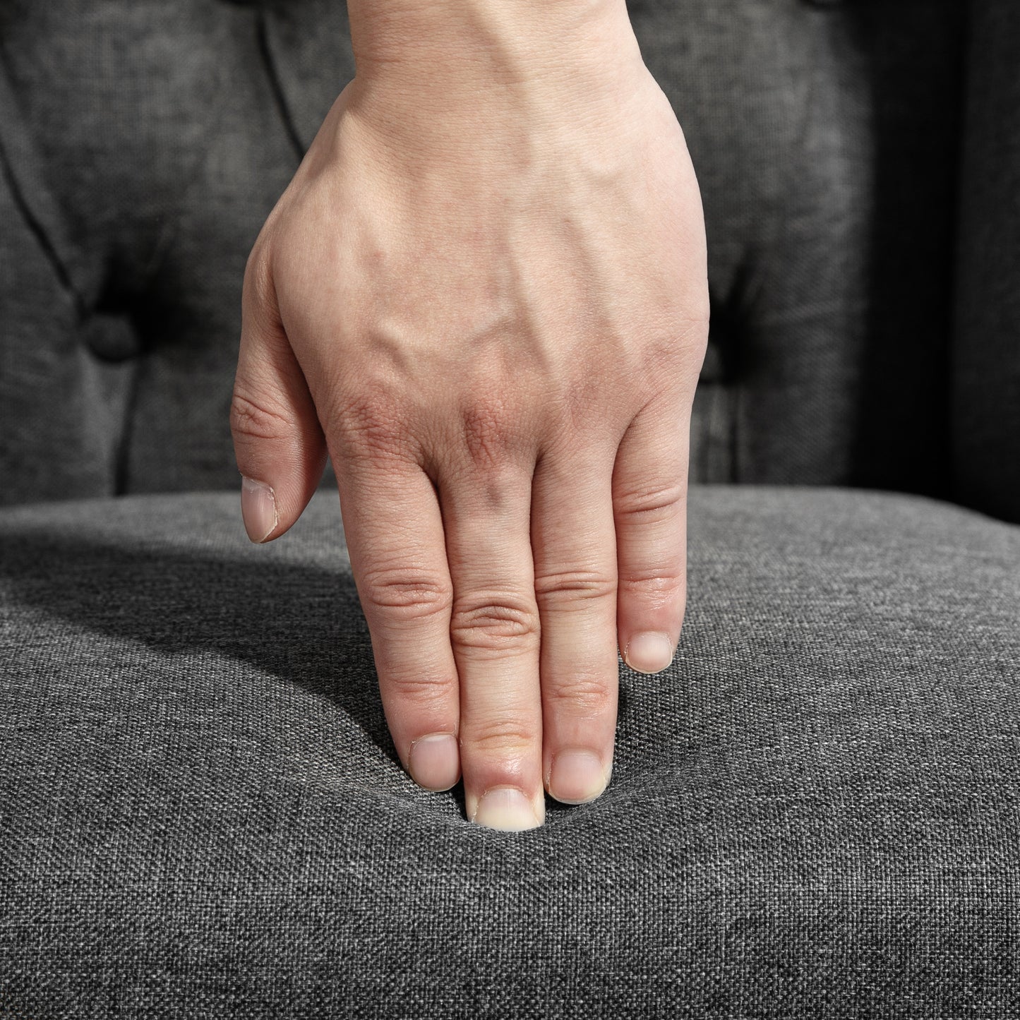 Hand pressing into a plush grey fabric sofa cushion for comfort test
