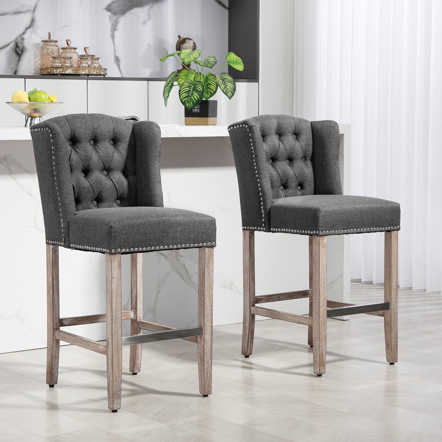 Two dark gray upholstered bar stools with tufted backs and nailhead trim on light wood legs