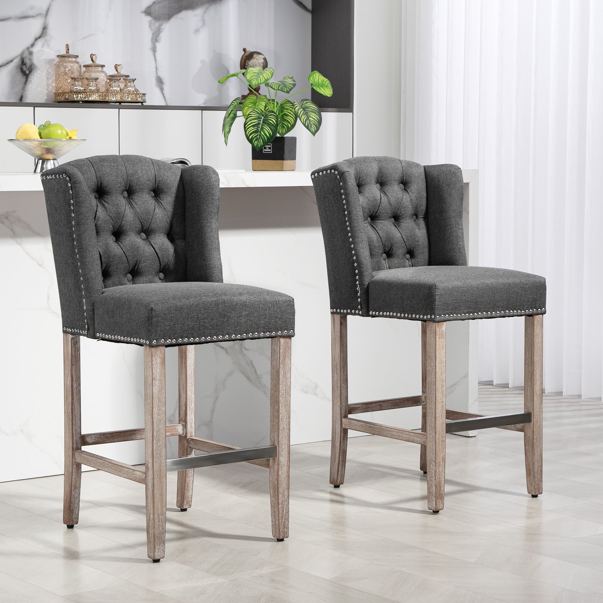 Two dark gray upholstered bar stools with tufted backs and nailhead trim on light wood legs