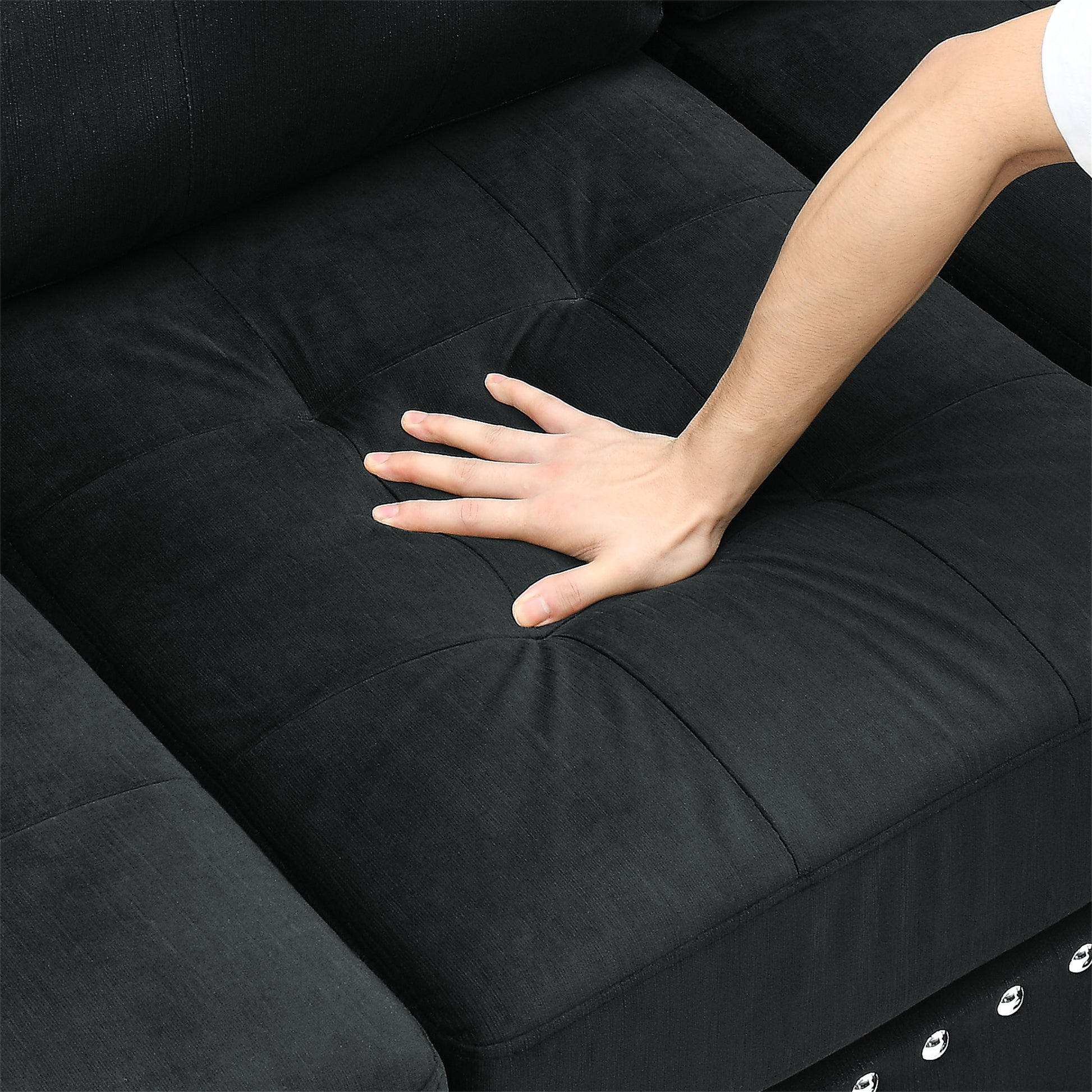 Closeup of a hand pressing into the plush black fabric of a tufted sofa cushion