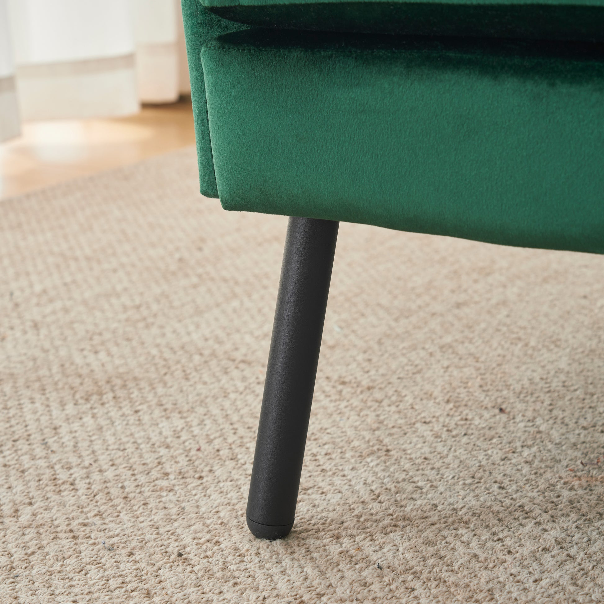 Deep green velvet sofa closeup showing luxurious texture and tapered black leg