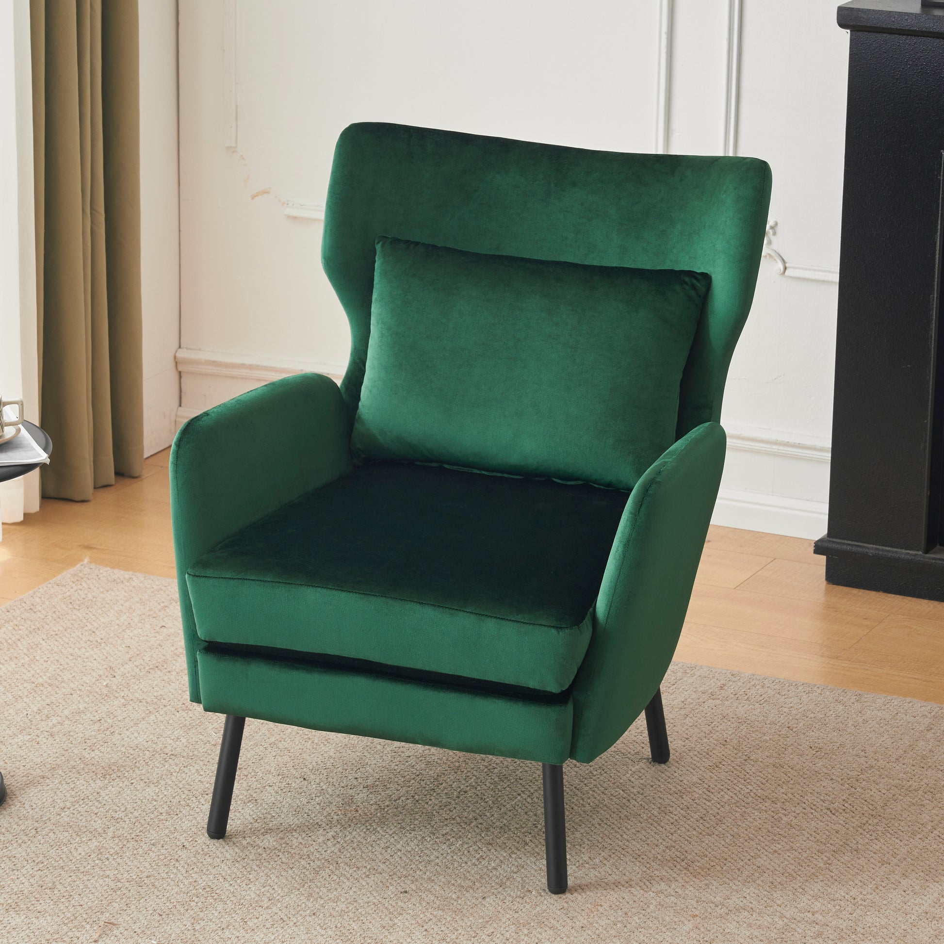 Plush emerald green velvet accent chair with a matching lumbar pillow and tapered black legs