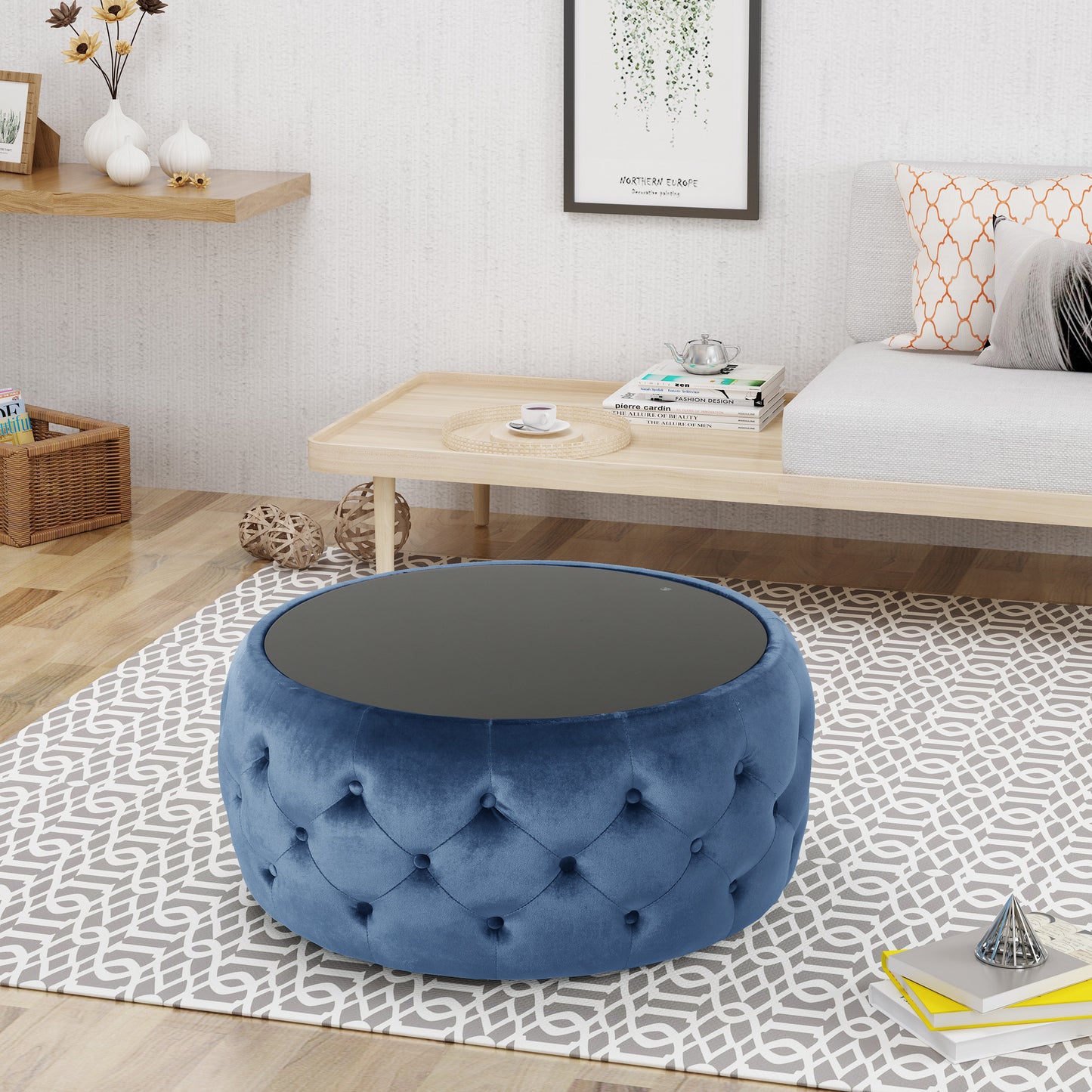 Blue velvet tufted ottoman with dark grey glass top on grey patterned rug