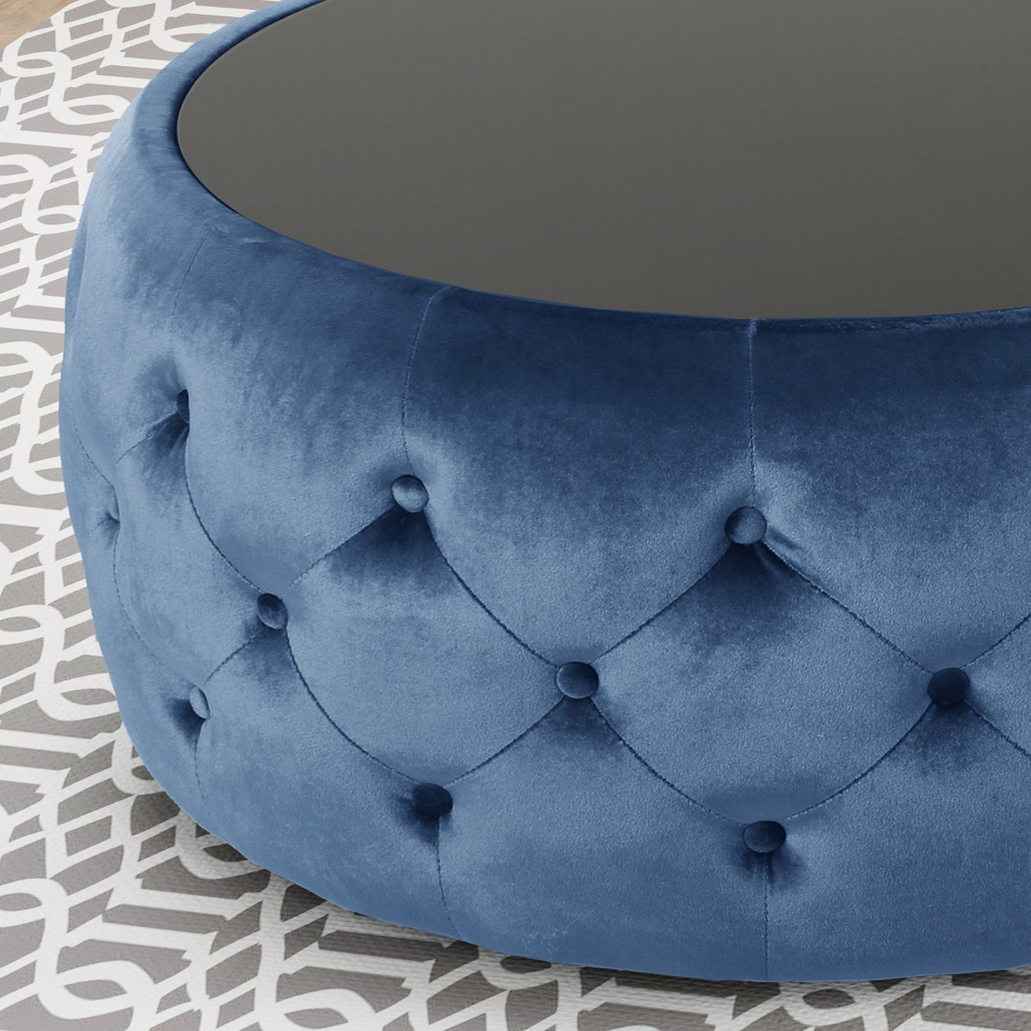 Plush blue velvet round ottoman with tufted detailing and a dark glass top