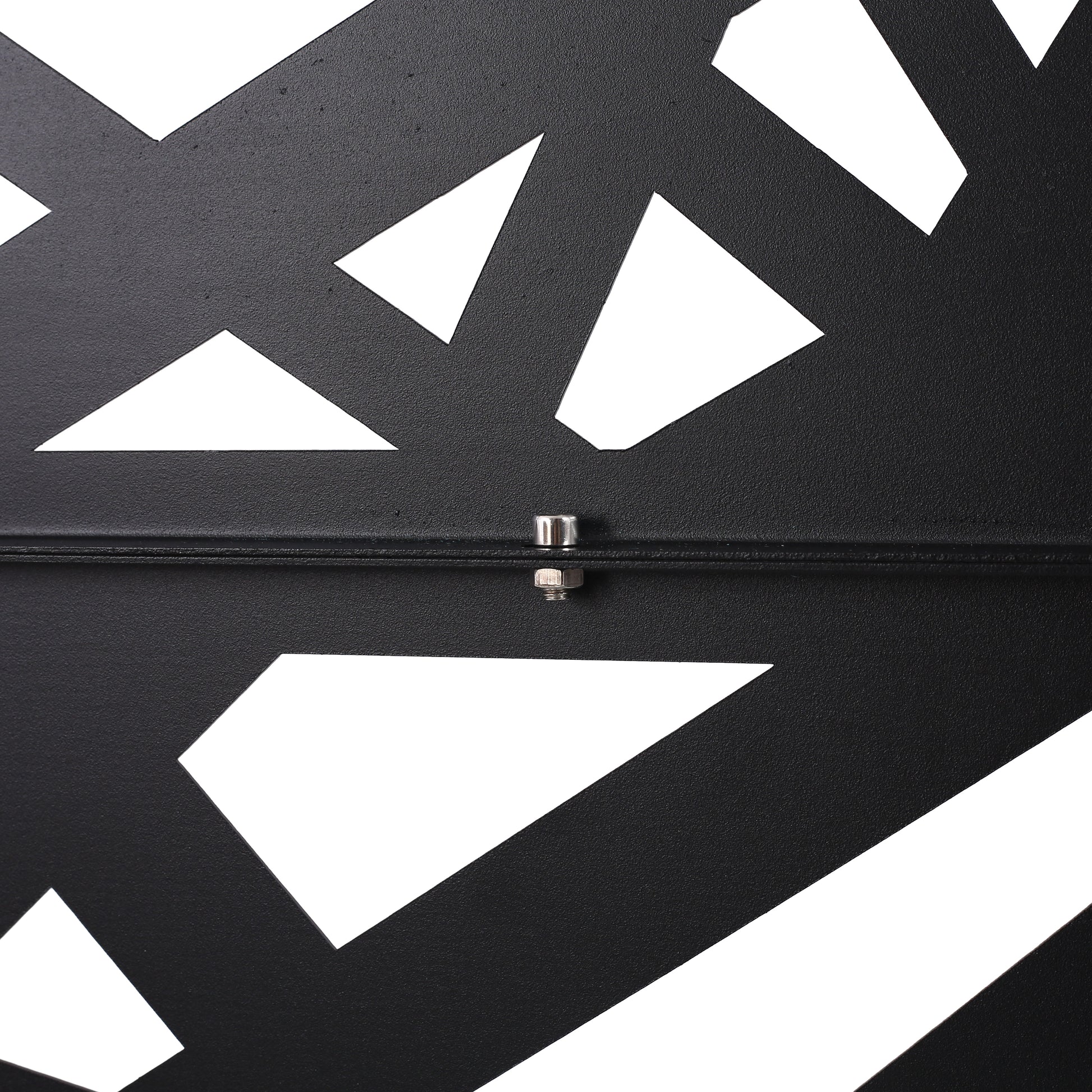 Closeup of a black metal decorative panel with abstract geometric cutouts and visible bolt