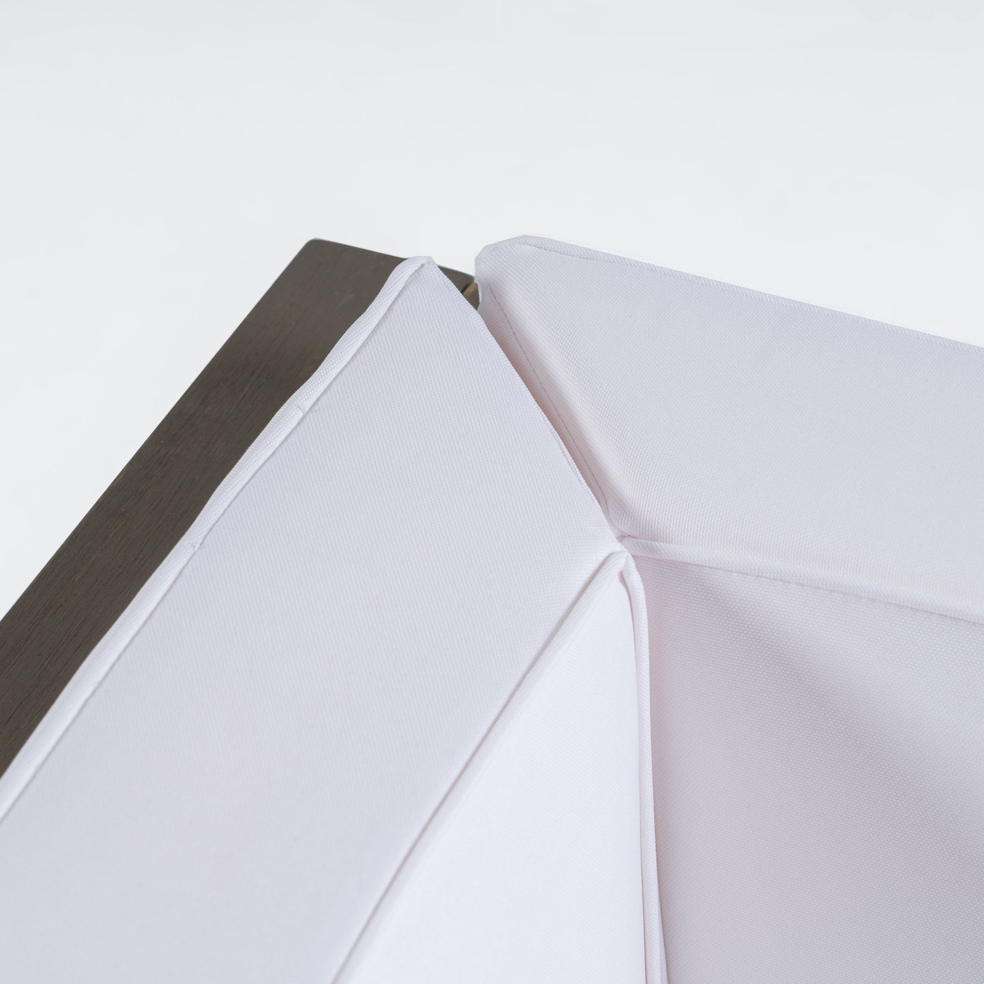 Closeup of a white textured outdoor cushion detail with a dark wooden frame edge