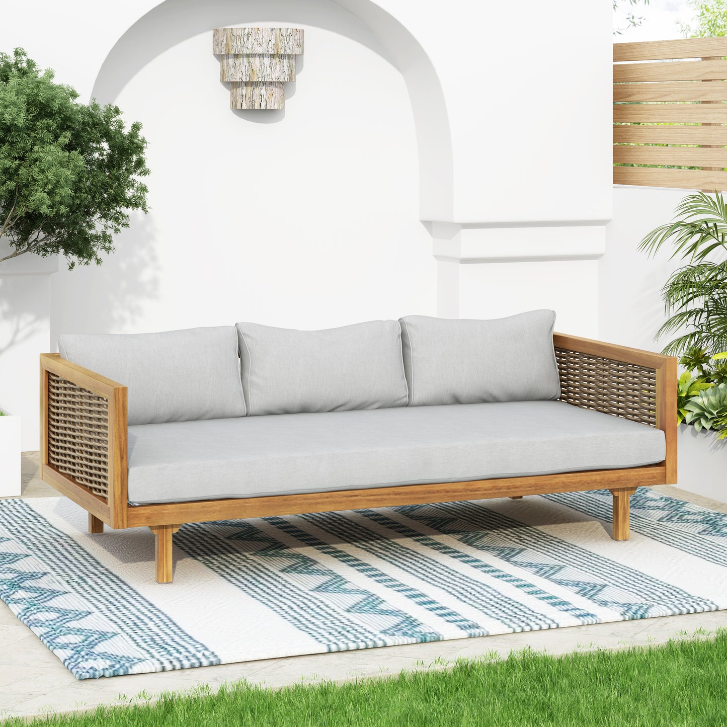 Teak and rattan outdoor sofa with light grey cushions on patterned rug