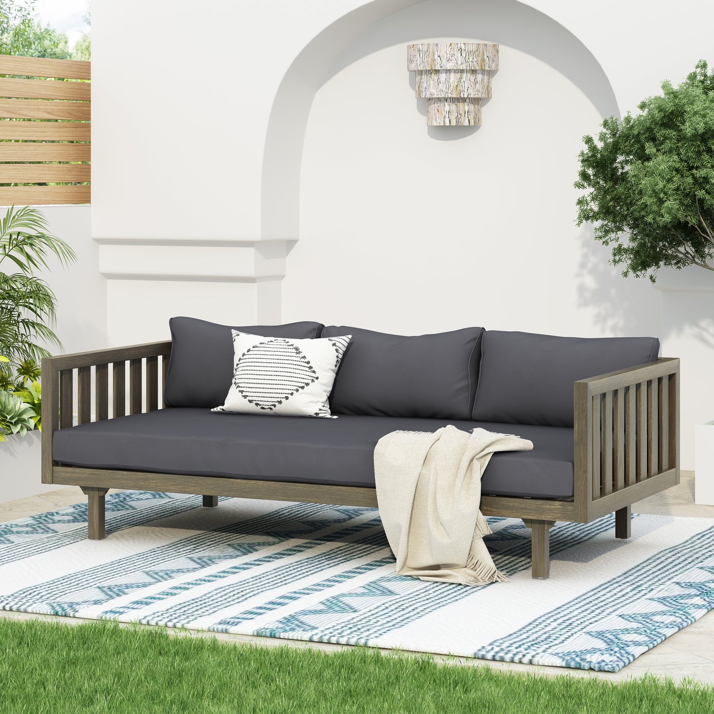 Dark gray upholstered outdoor daybed with wooden frame and geometric throw pillow