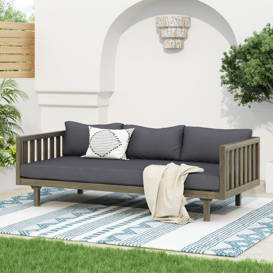 Dark gray upholstered outdoor daybed with wooden frame and geometric throw pillow
