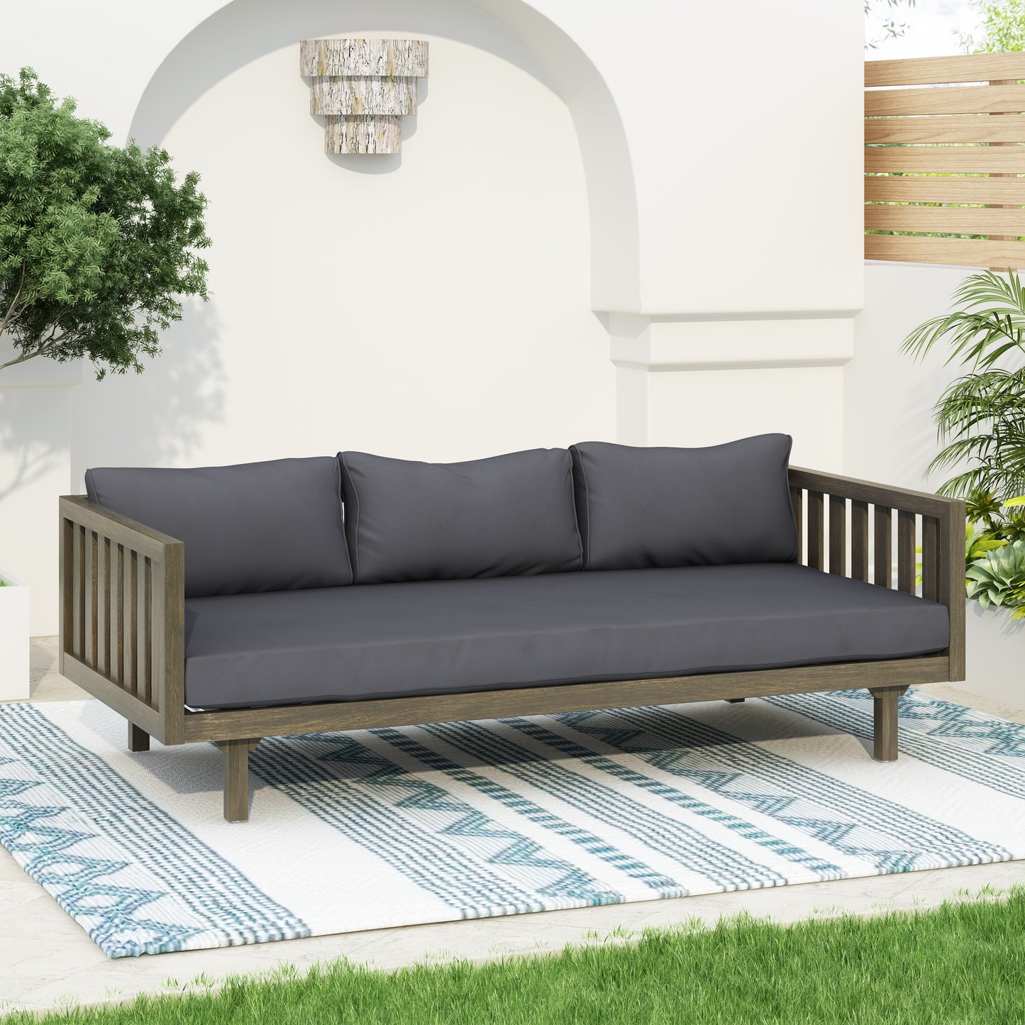 Gray upholstered outdoor daybed with a weathered wood frame sits on a patterned rug